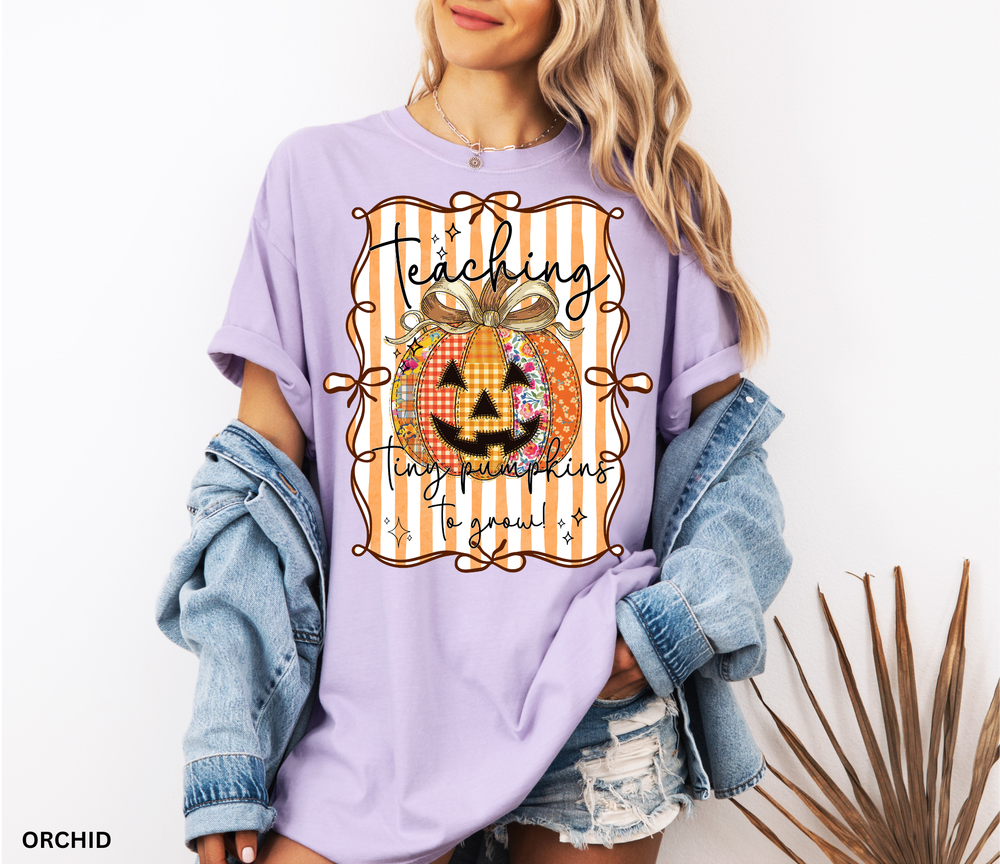 Halloween teacher shirt with an orange patchwork jack-o’-lantern tied in a bow on a striped background and the phrase “Teaching Tiny Pumpkins to Grow.”