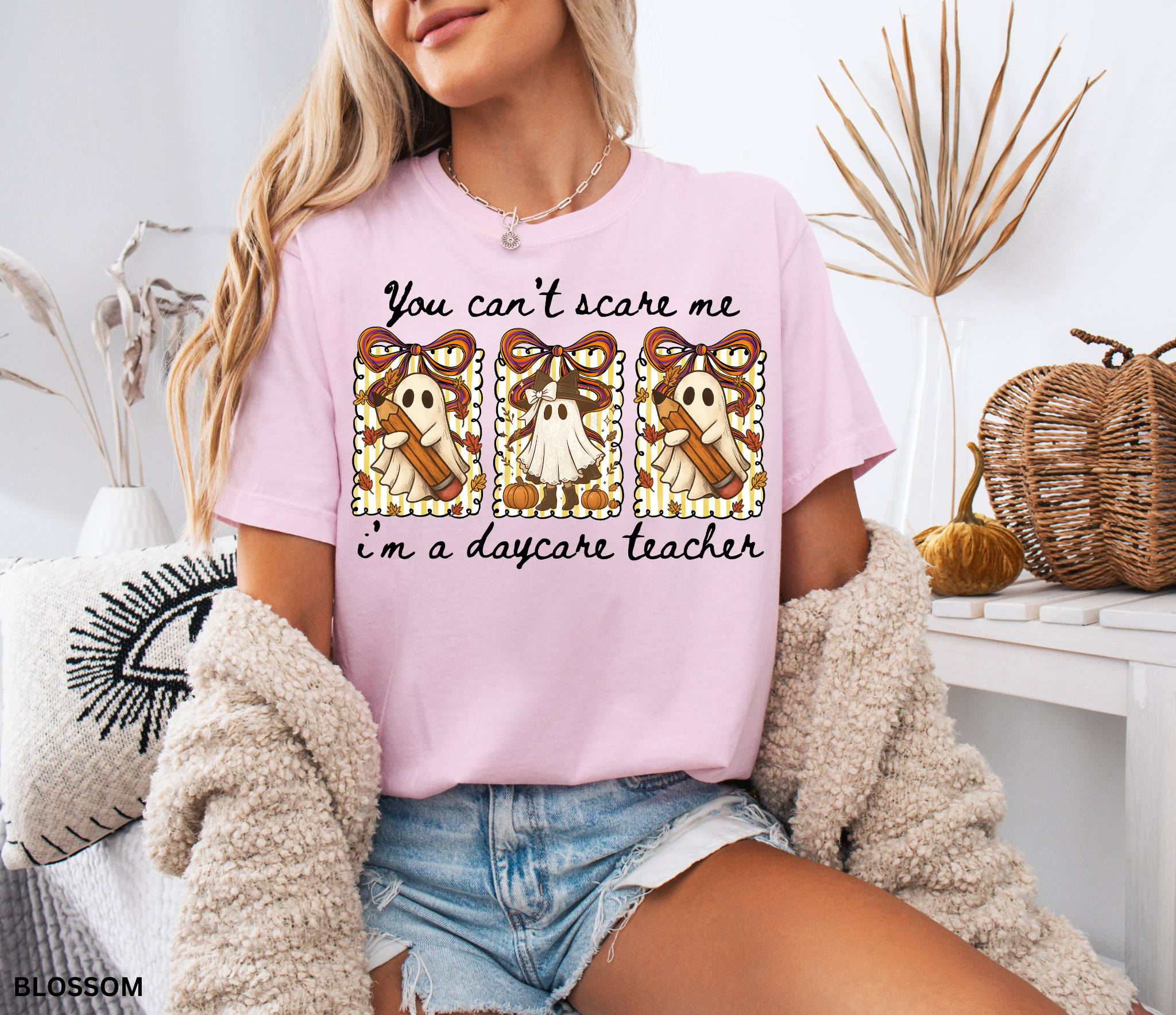 Halloween daycare teacher shirt with three cute ghosts holding pencils and pumpkins, decorated with striped backgrounds, bows, and the phrase “You Can’t Scare Me, I’m a Daycare Teacher.”