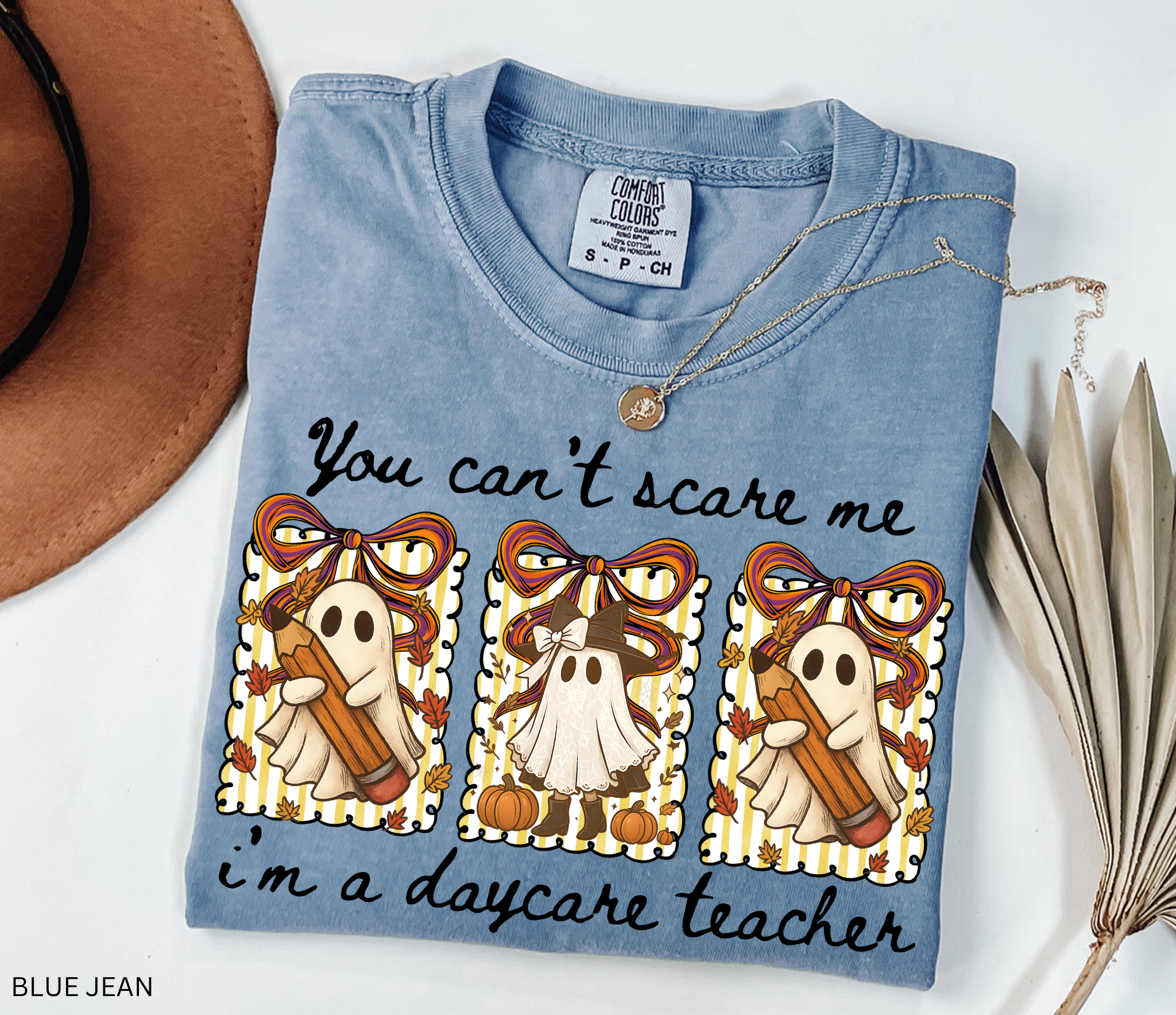 Halloween daycare teacher shirt with three cute ghosts holding pencils and pumpkins, decorated with striped backgrounds, bows, and the phrase “You Can’t Scare Me, I’m a Daycare Teacher.”