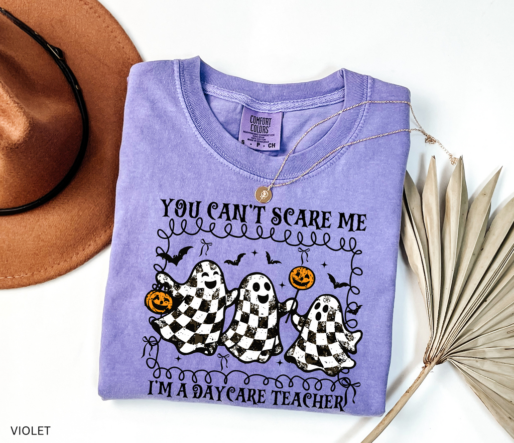 Daycare teacher Halloween shirt with three black and white checkered ghosts holding pumpkins and candy, surrounded by bats in a playful spooky design.