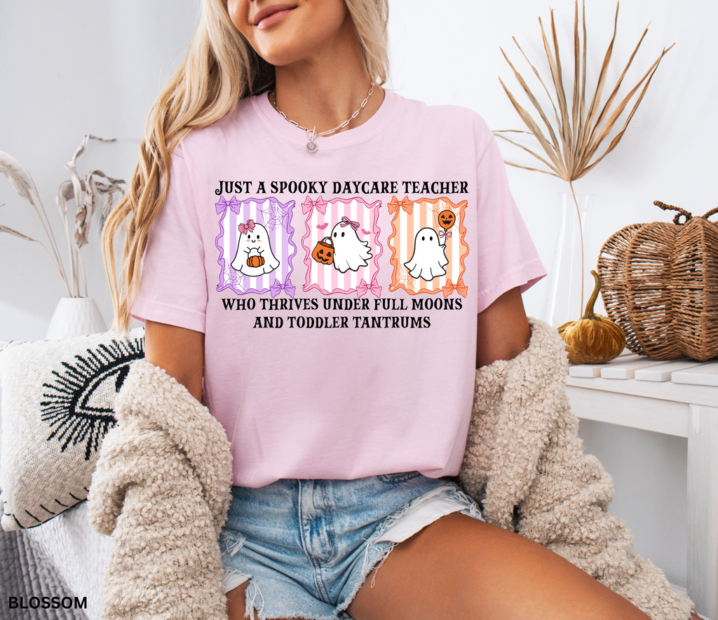 Daycare teacher Halloween shirt with three pastel ghosts holding pumpkins and candy, surrounded by bows and spiderwebs, with the phrase “Just a Spooky Daycare Teacher Who Thrives Under Full Moons and Toddler Tantrums.”
