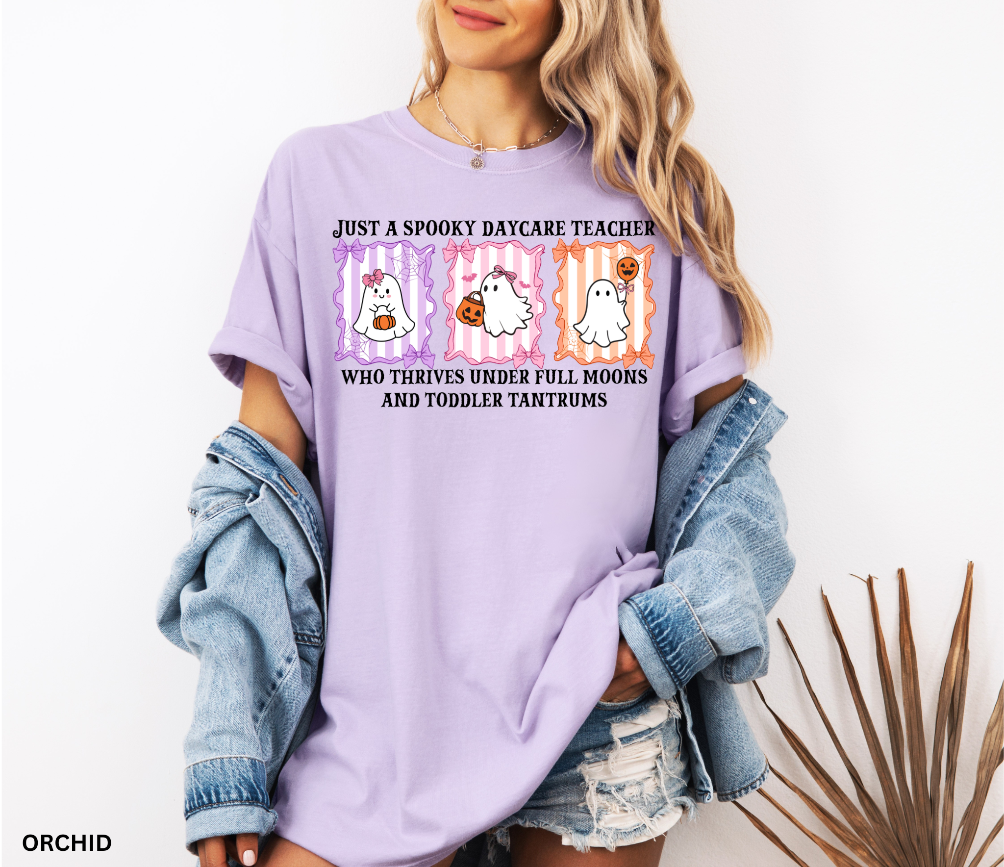 Daycare teacher Halloween shirt with three pastel ghosts holding pumpkins and candy, surrounded by bows and spiderwebs, with the phrase “Just a Spooky Daycare Teacher Who Thrives Under Full Moons and Toddler Tantrums.”