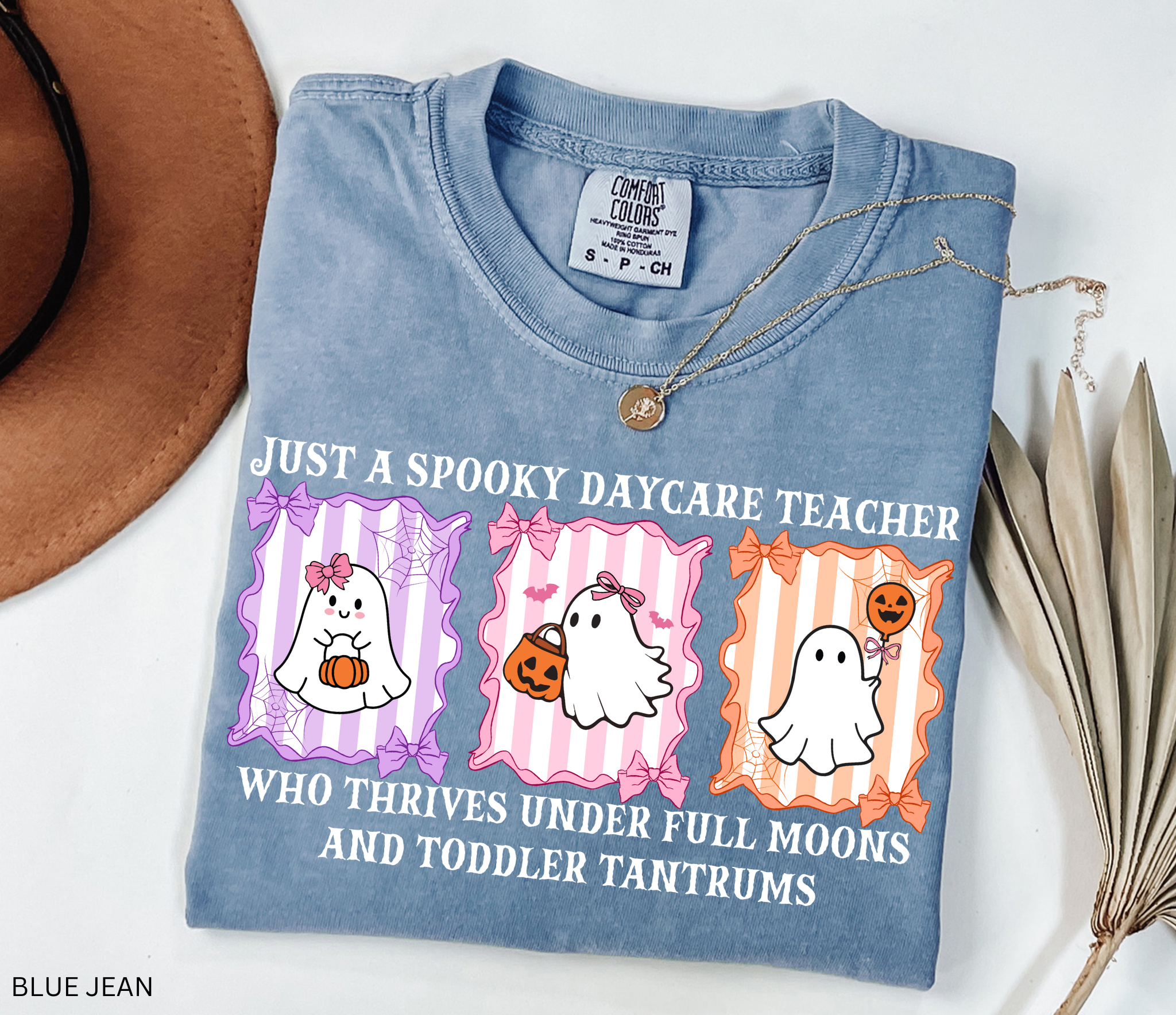 Daycare teacher Halloween shirt with three pastel ghosts holding pumpkins and candy, surrounded by bows and spiderwebs, with the phrase “Just a Spooky Daycare Teacher Who Thrives Under Full Moons and Toddler Tantrums.”