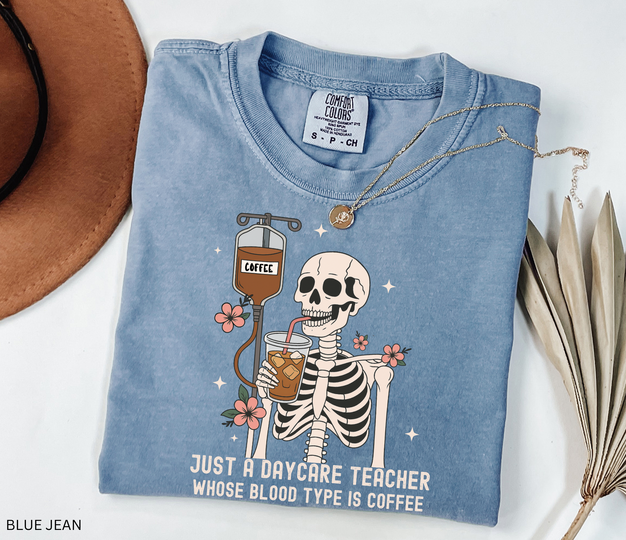 Daycare teacher Halloween shirt with a skeleton sipping iced coffee through a straw connected to an IV bag labeled “coffee,” surrounded by flowers and stars.