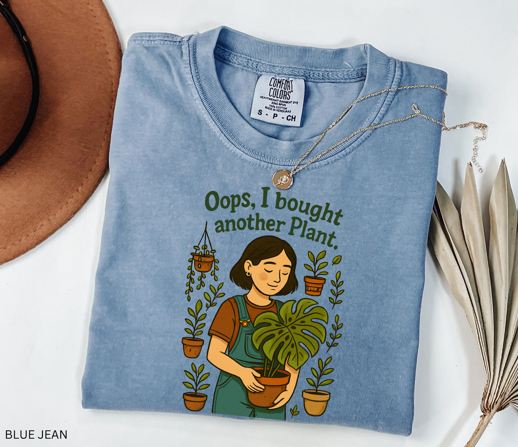 Gardening shirt with a woman in overalls holding a monstera plant, surrounded by potted plants, with the phrase “Oops, I Bought Another Plant.”