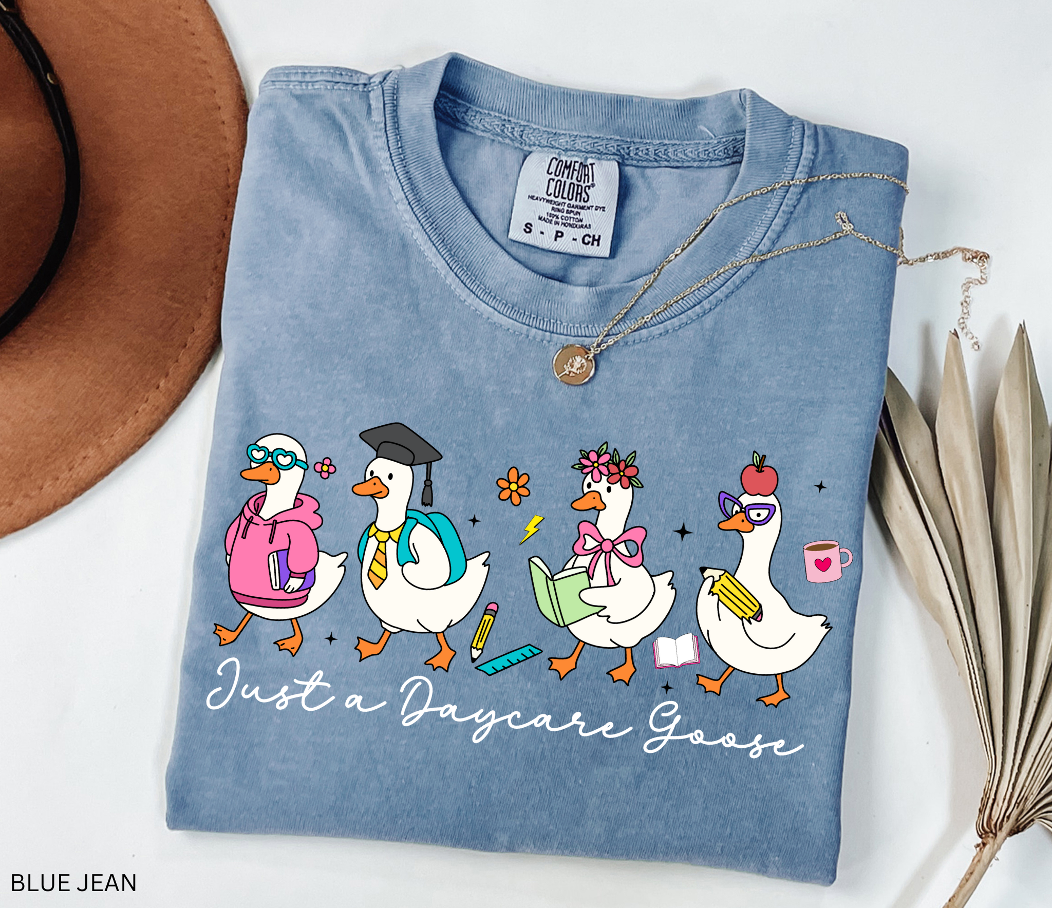 Funny daycare teacher shirt with four cartoon geese dressed as students and teachers, holding books and supplies, with the phrase “Just a Daycare Goose.”