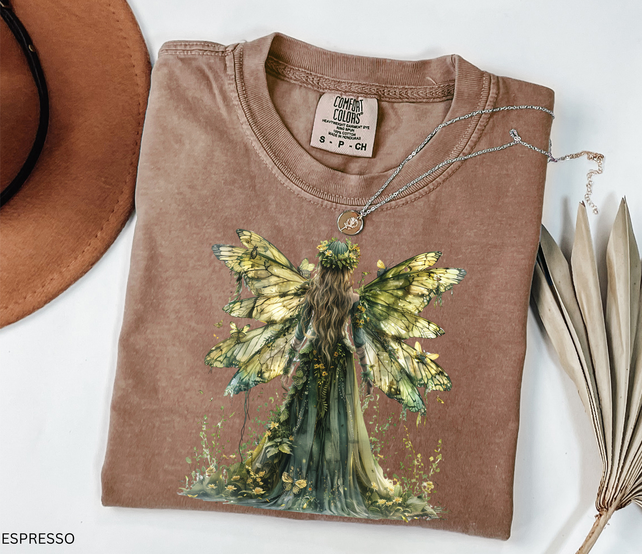 Watercolor-style illustration of a fairy with large golden butterfly wings and a flowing green gown, surrounded by flowers and plants, printed on a cottagecore t-shirt.