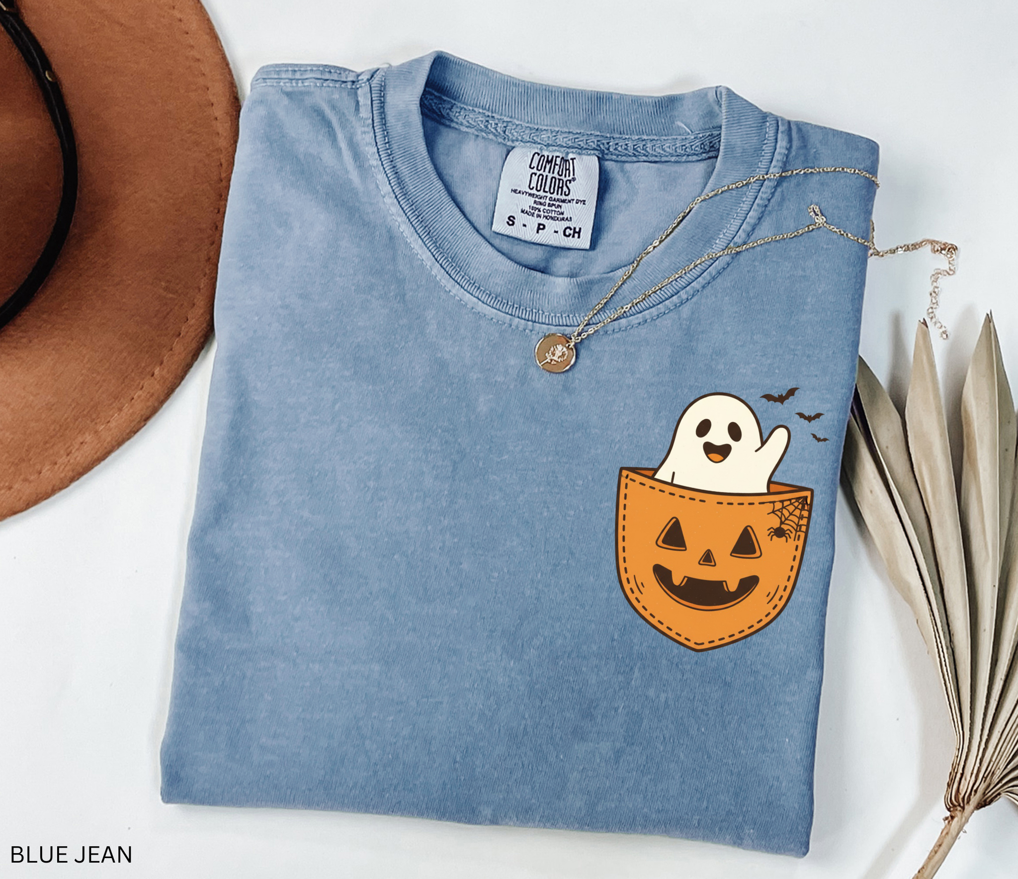 Cute ghost peeking out of a jack-o’-lantern pocket with bats and spiderweb detail on a Halloween t-shirt.