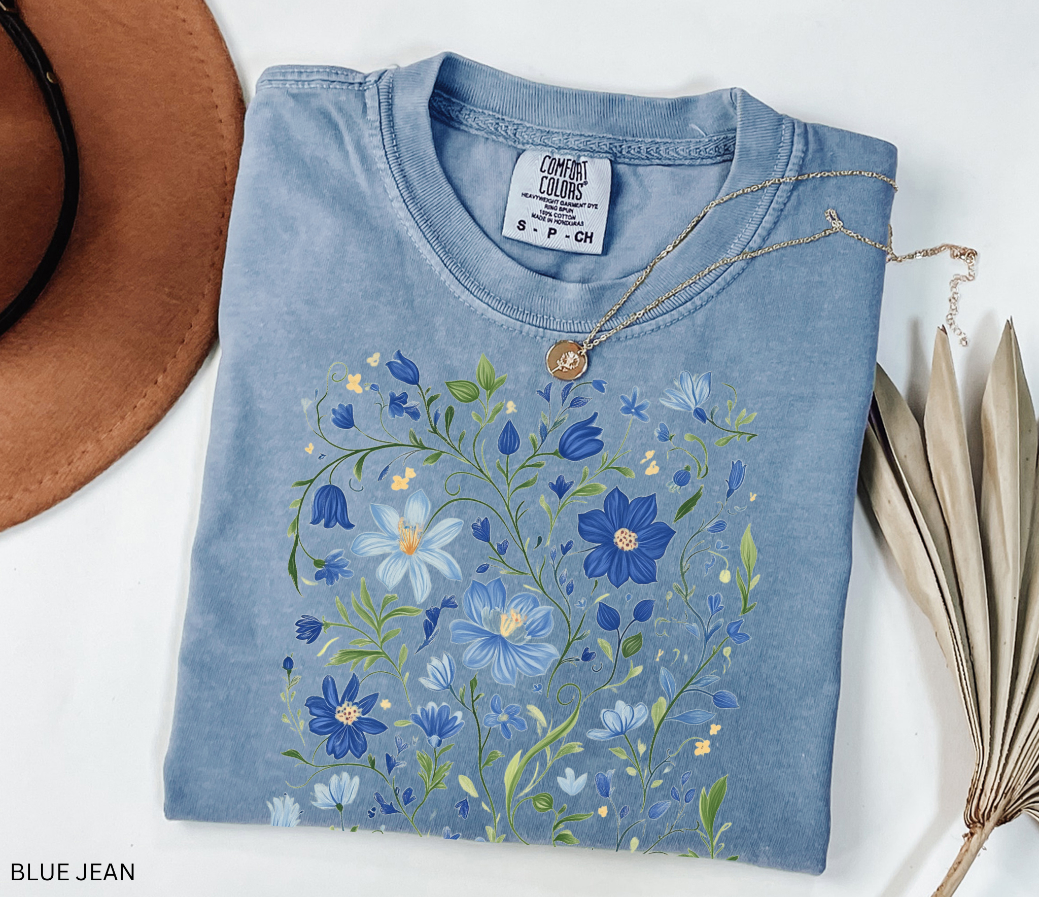 Detailed folk-art style design of blue wildflowers and green vines, printed on a cottagecore floral t-shirt.