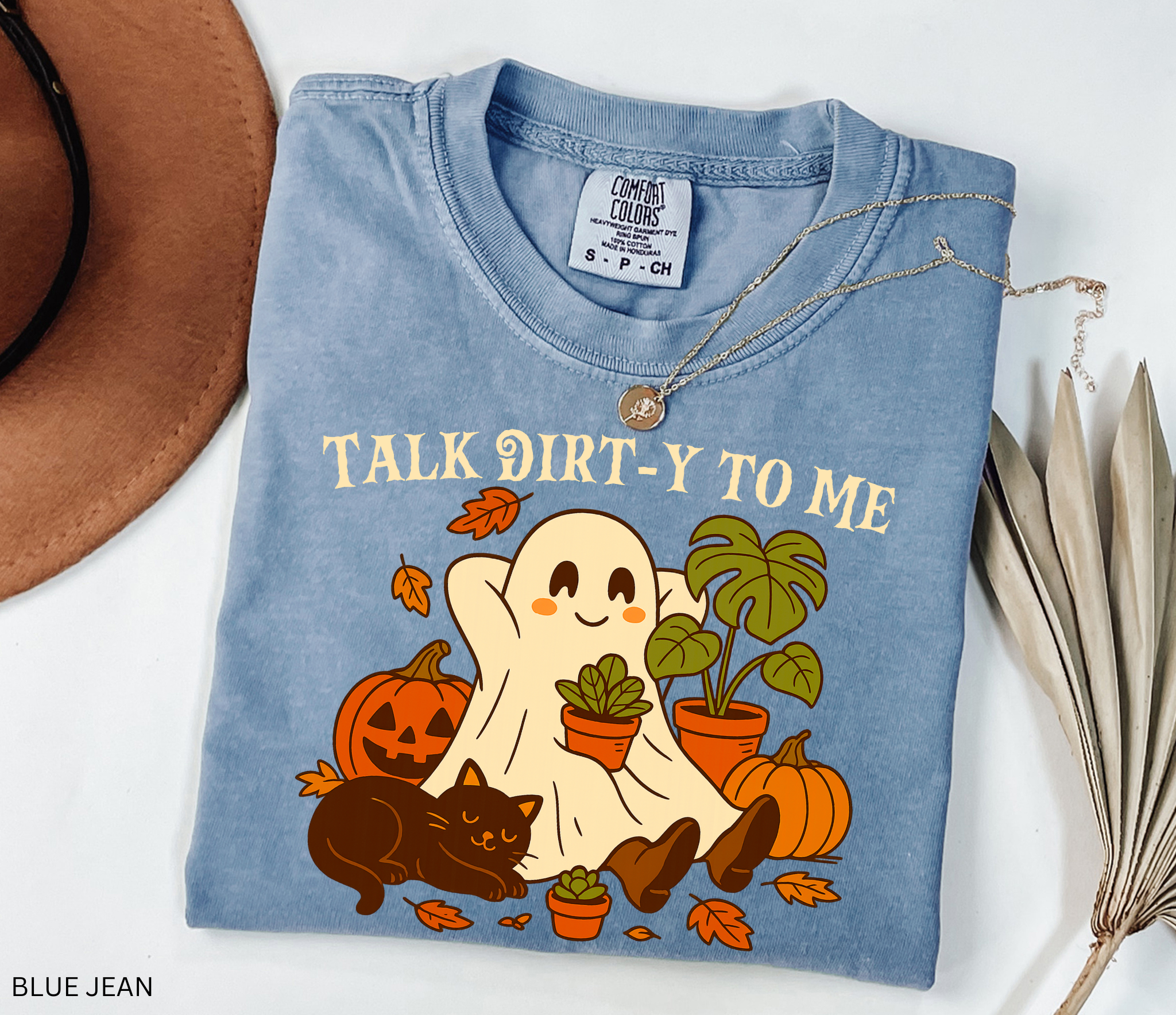 Halloween shirt design featuring a happy ghost holding a potted plant, surrounded by pumpkins, autumn leaves, a monstera, and a cozy black cat with the phrase “Talk Dirt-y to Me.”