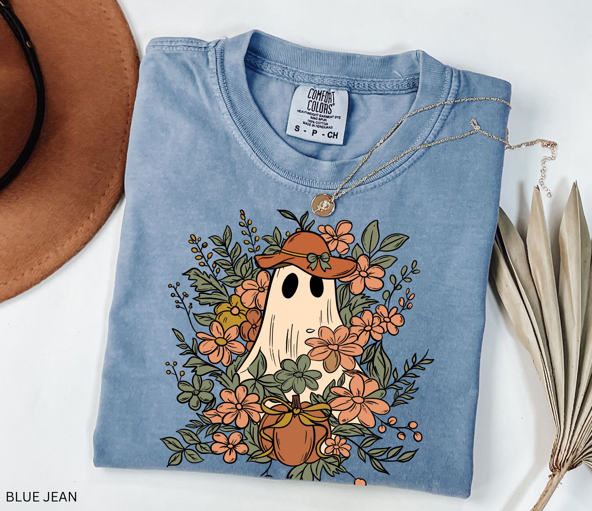 Halloween shirt featuring a ghost in a wide-brimmed hat surrounded by orange flowers, greenery, and a pumpkin with a bow – a spooky cottagecore gardening design.
