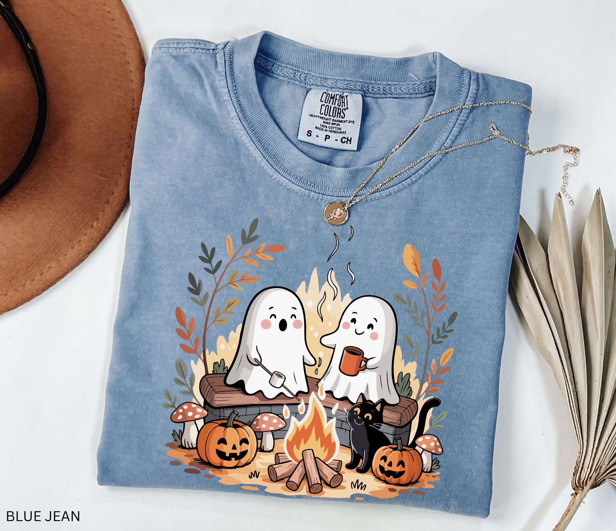 Halloween shirt design featuring two cute ghosts by a campfire, one roasting marshmallows, one holding cocoa, with pumpkins, mushrooms, fall leaves, and a black cat.