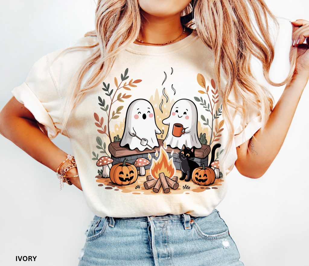 Halloween shirt design featuring two cute ghosts by a campfire, one roasting marshmallows, one holding cocoa, with pumpkins, mushrooms, fall leaves, and a black cat.