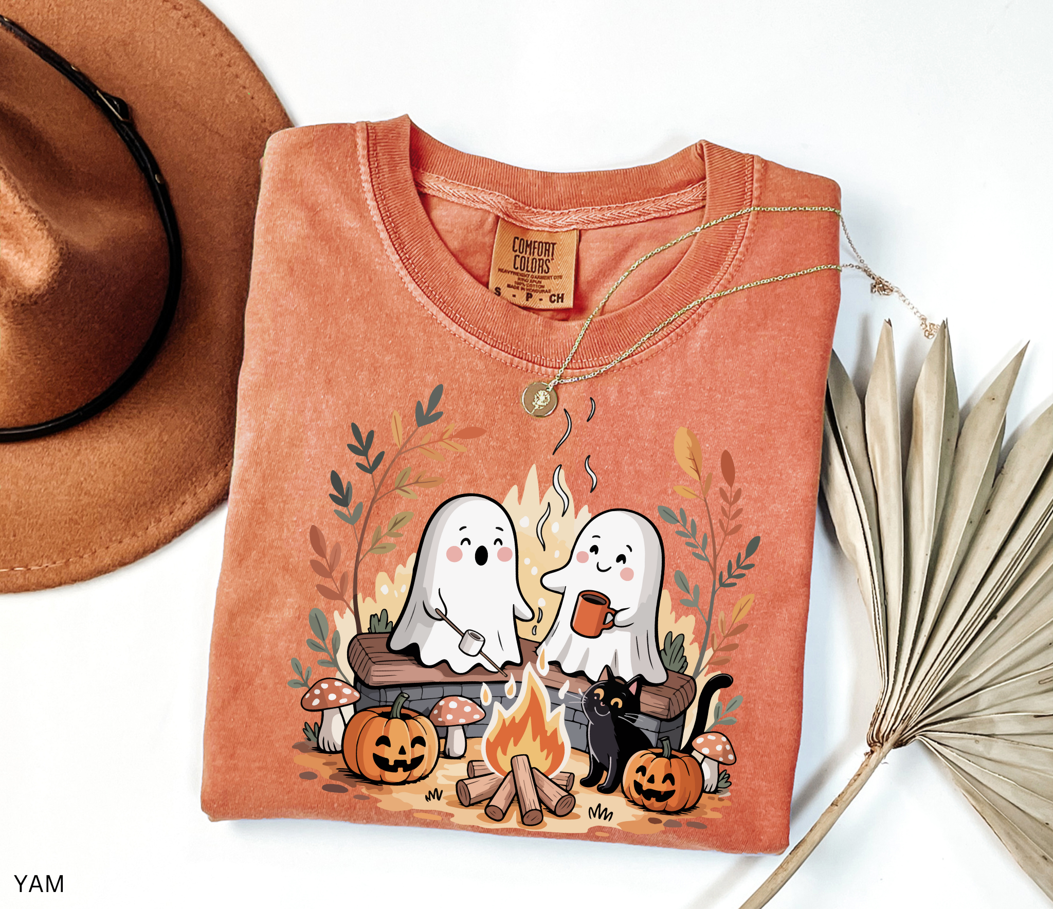 Halloween shirt design featuring two cute ghosts by a campfire, one roasting marshmallows, one holding cocoa, with pumpkins, mushrooms, fall leaves, and a black cat.