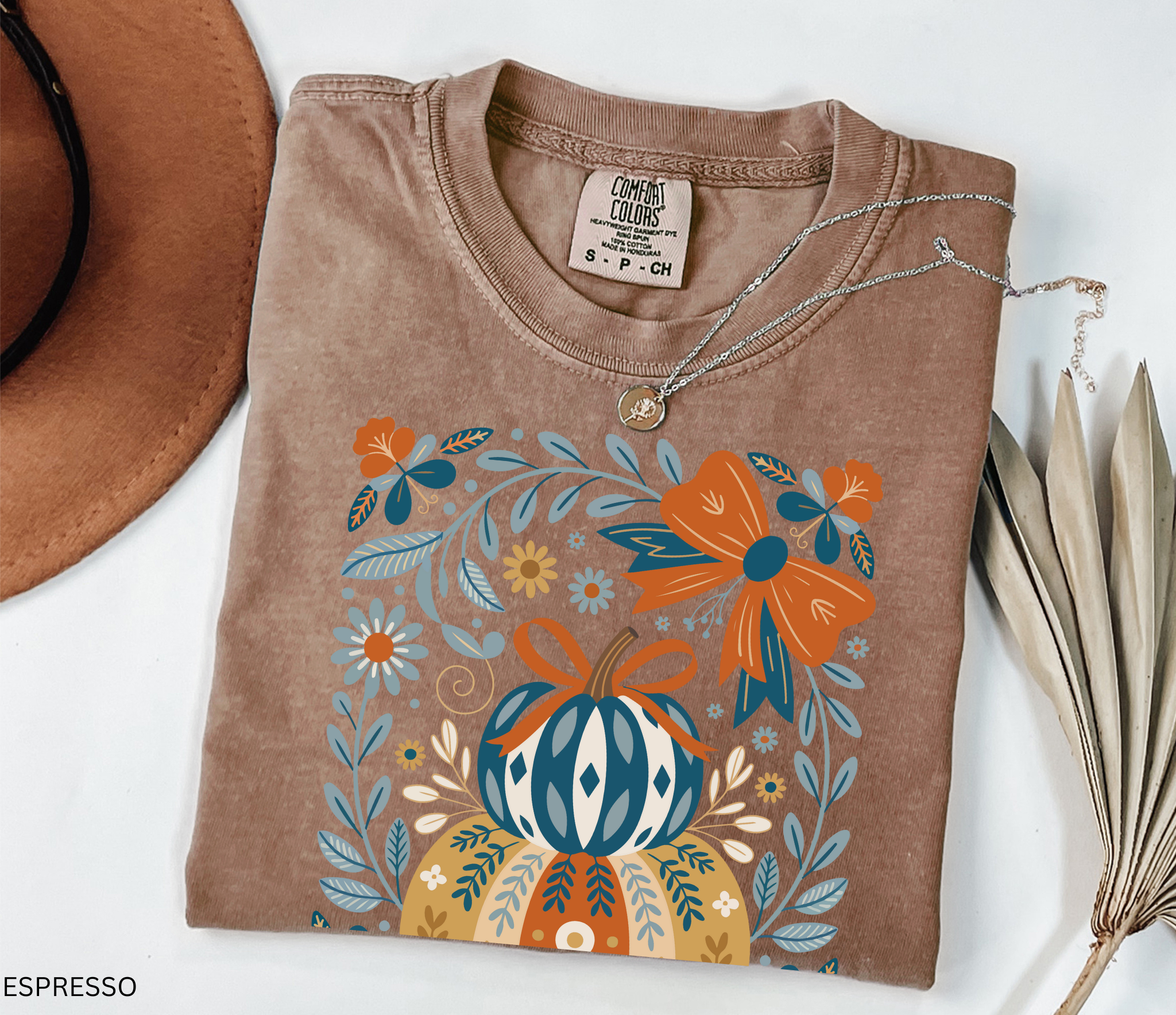 Whimsical folk art pumpkin with bow and floral details in warm autumn colors, printed as a cottagecore fall design on a t-shirt.