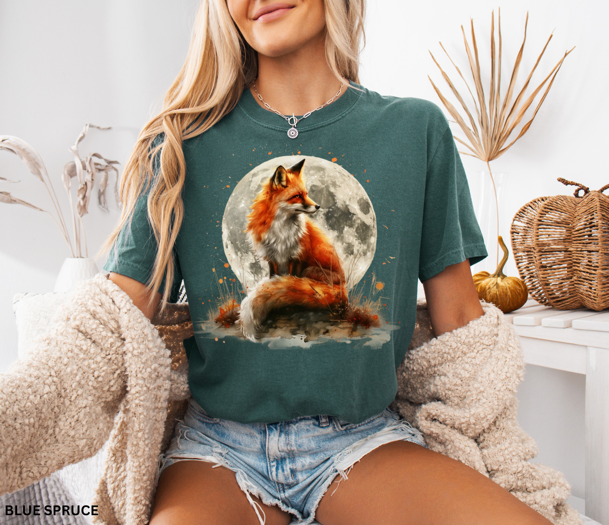 Watercolor-style illustration of a fox sitting beneath a glowing full moon, surrounded by grass and earthy details on a cottagecore shirt.