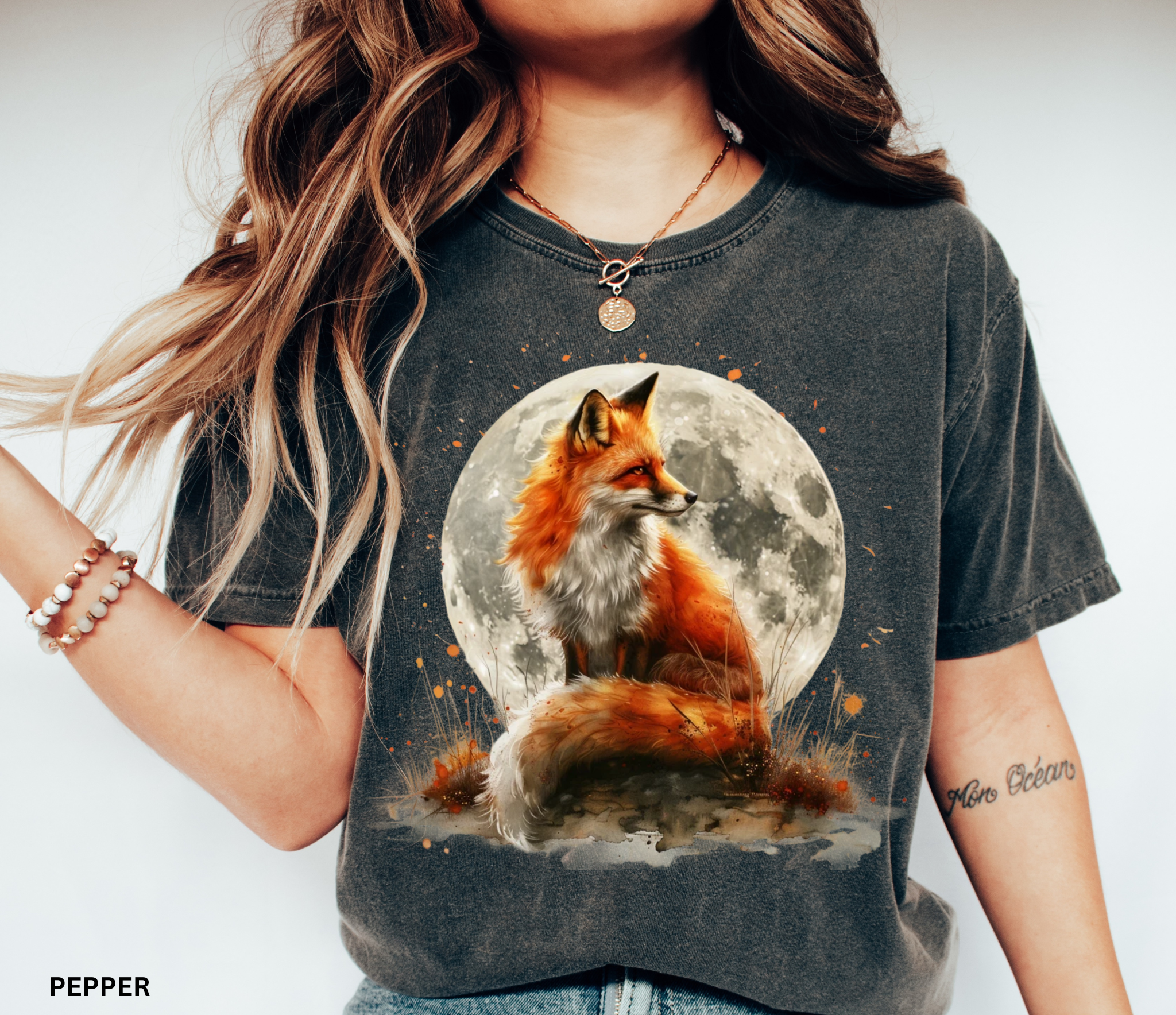 Watercolor-style illustration of a fox sitting beneath a glowing full moon, surrounded by grass and earthy details on a cottagecore shirt.