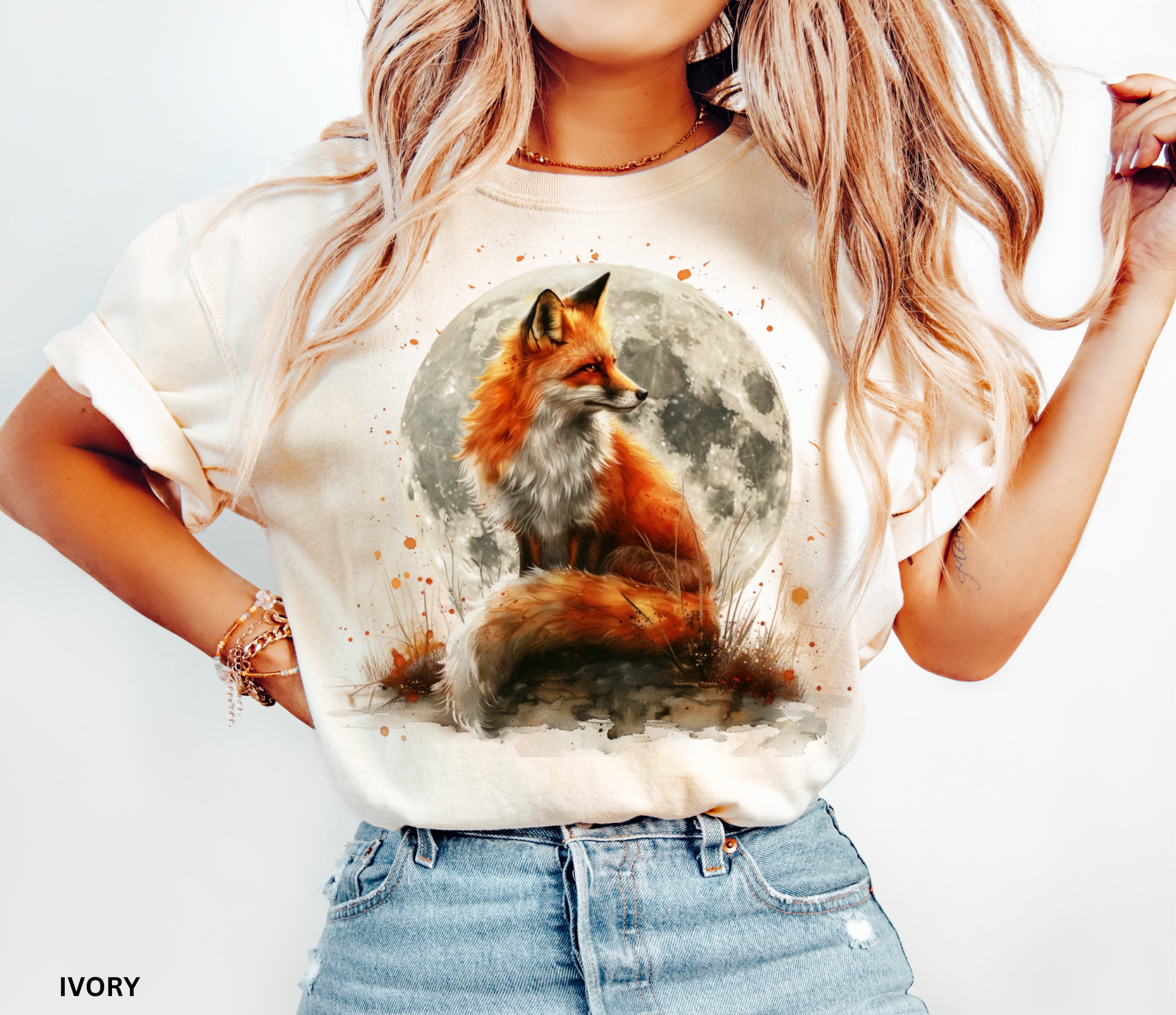 Watercolor-style illustration of a fox sitting beneath a glowing full moon, surrounded by grass and earthy details on a cottagecore shirt.
