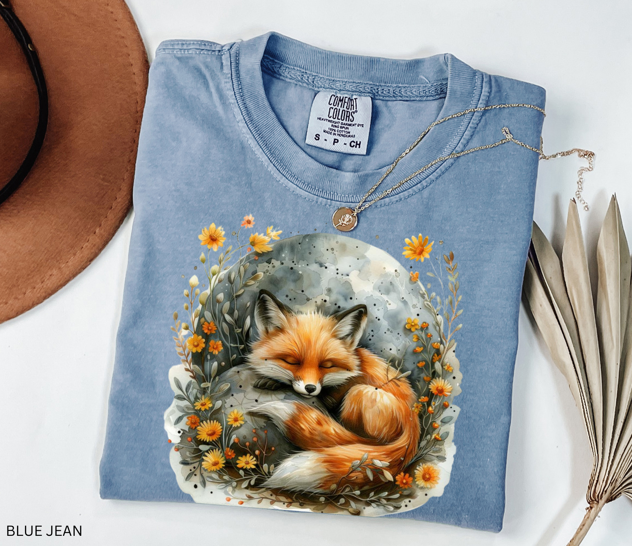 Illustration of a sleeping fox curled beneath a glowing moon, surrounded by golden wildflowers and soft foliage on a cottagecore shirt.