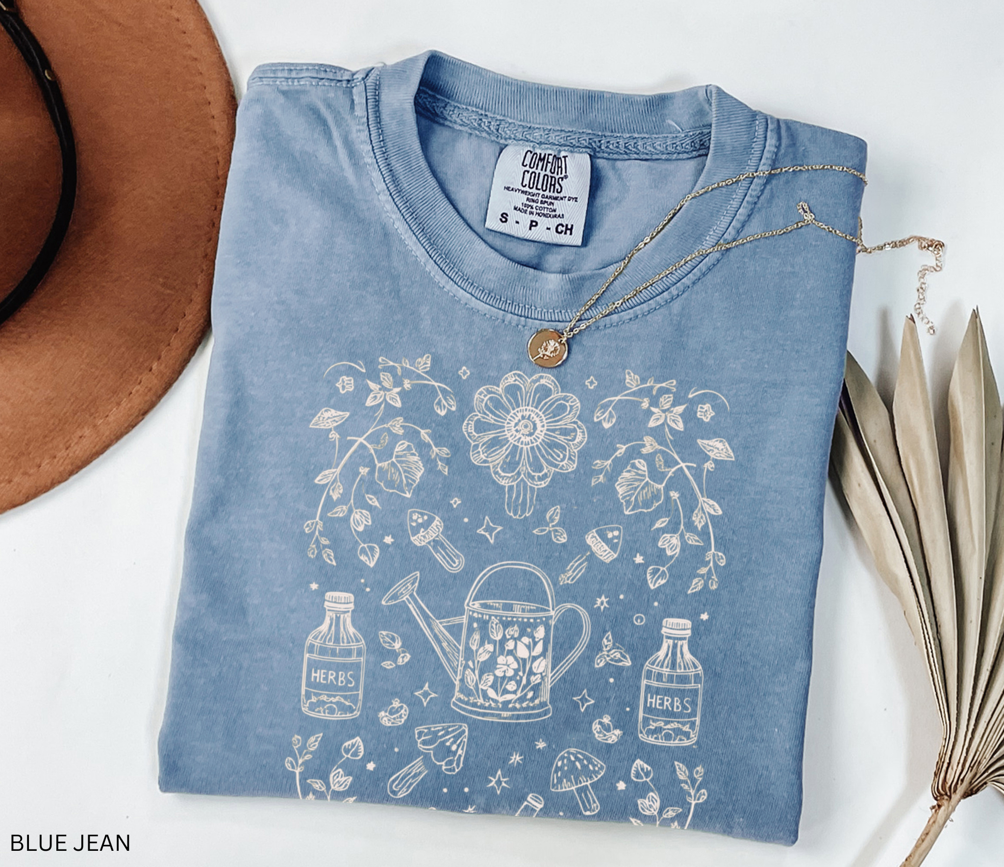 Hand-drawn herbal apothecary t-shirt featuring vintage bottles, mushrooms, watering can, and mortar and pestle — botanical witch aesthetic on Comfort Colors shirt.