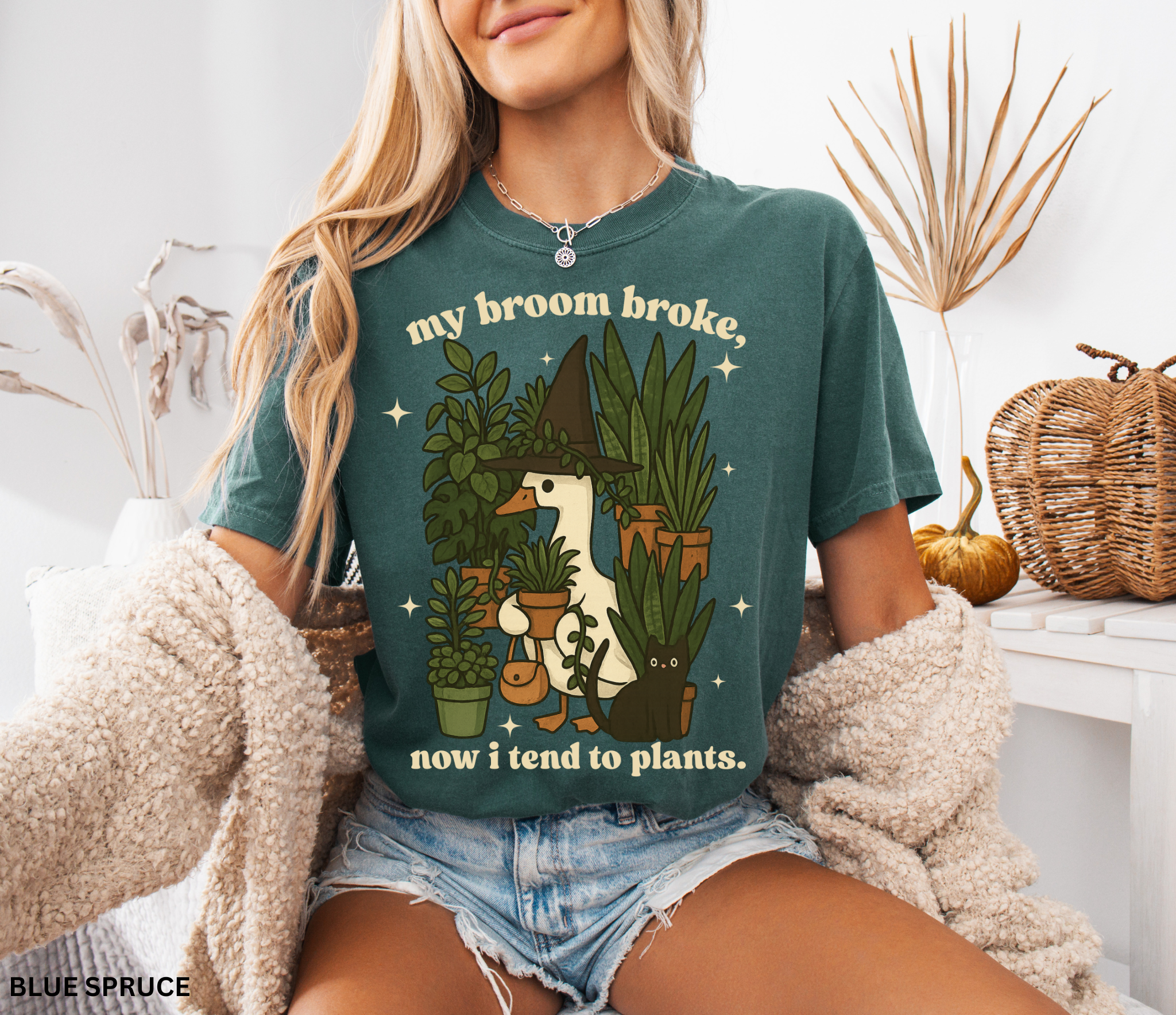 Witchy goose holding plants with a black cat surrounded by greenery — “My broom broke, now I tend to plants” text on cozy Comfort Colors tee.