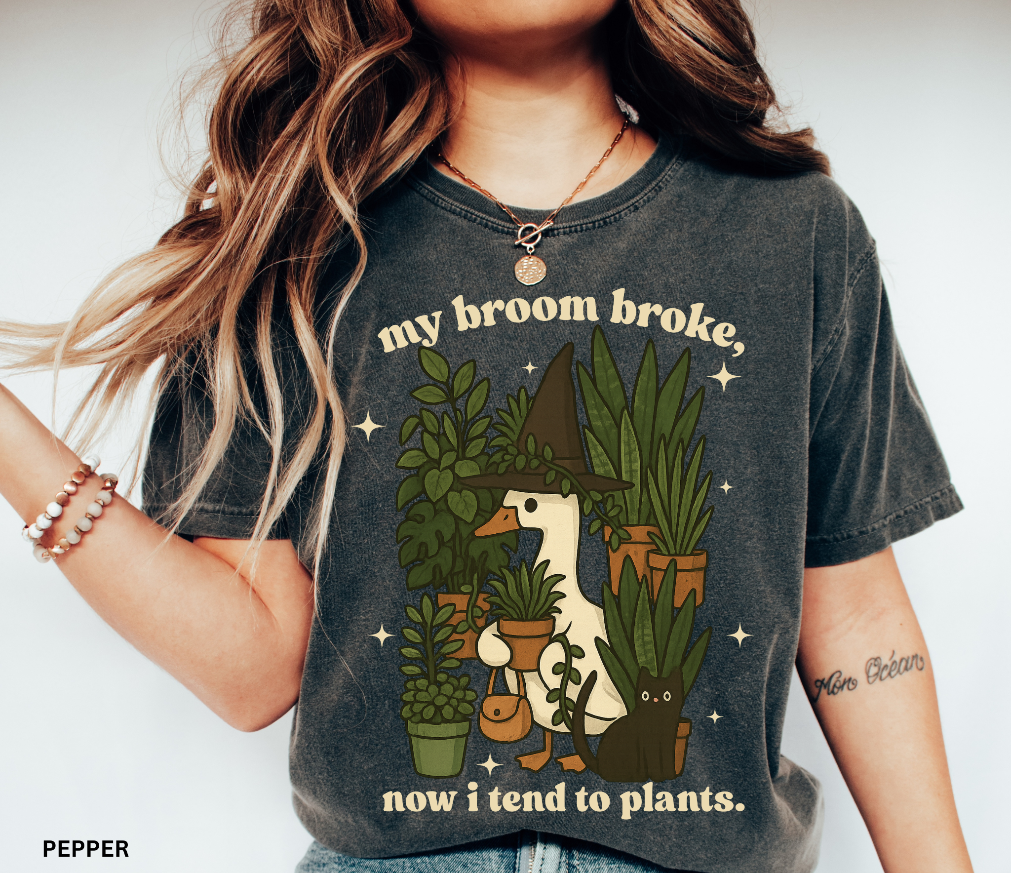 Witchy goose holding plants with a black cat surrounded by greenery — “My broom broke, now I tend to plants” text on cozy Comfort Colors tee.