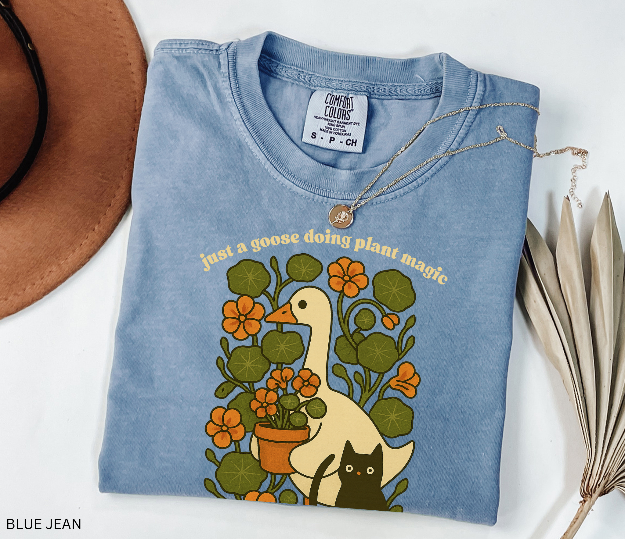 Goose holding a pot of nasturtiums with black cat among orange flowers — cozy cottagecore witchy plant lover shirt.