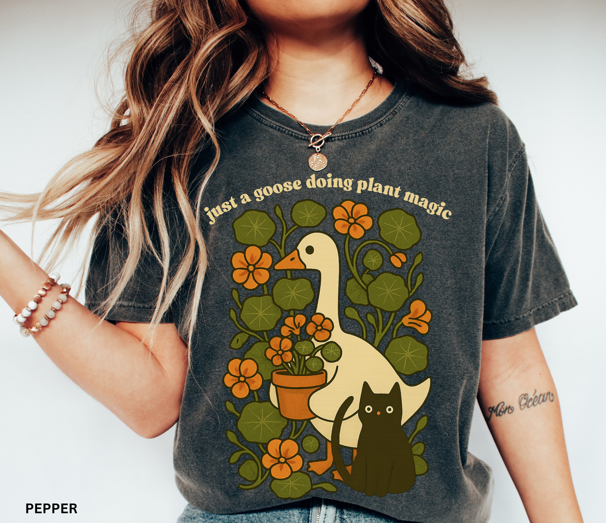 Goose holding a pot of nasturtiums with black cat among orange flowers — cozy cottagecore witchy plant lover shirt.