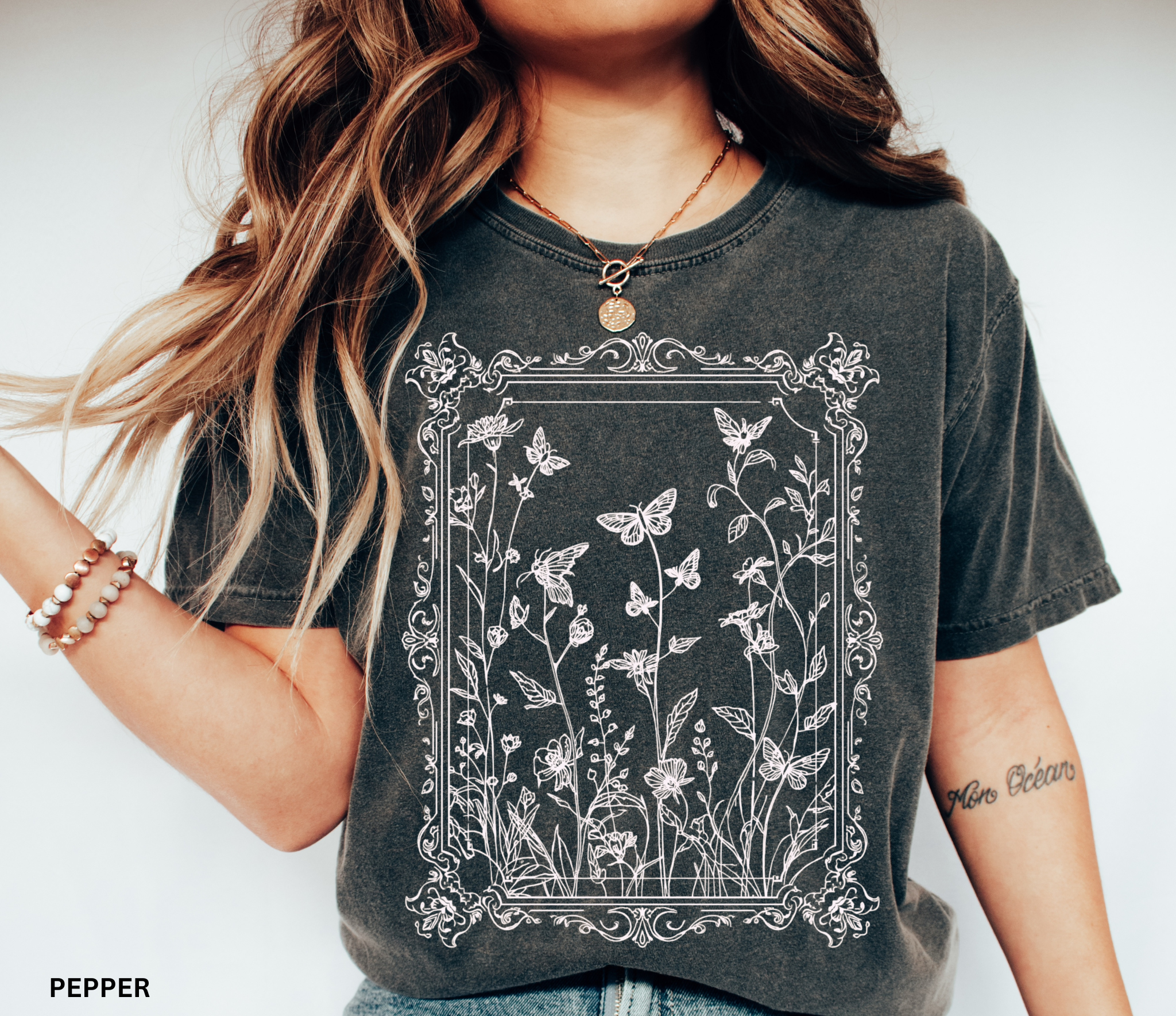 An ornate Victorian-style frame encasing hand-drawn butterflies and wildflowers on a whimsigoth-inspired cottagecore shirt.