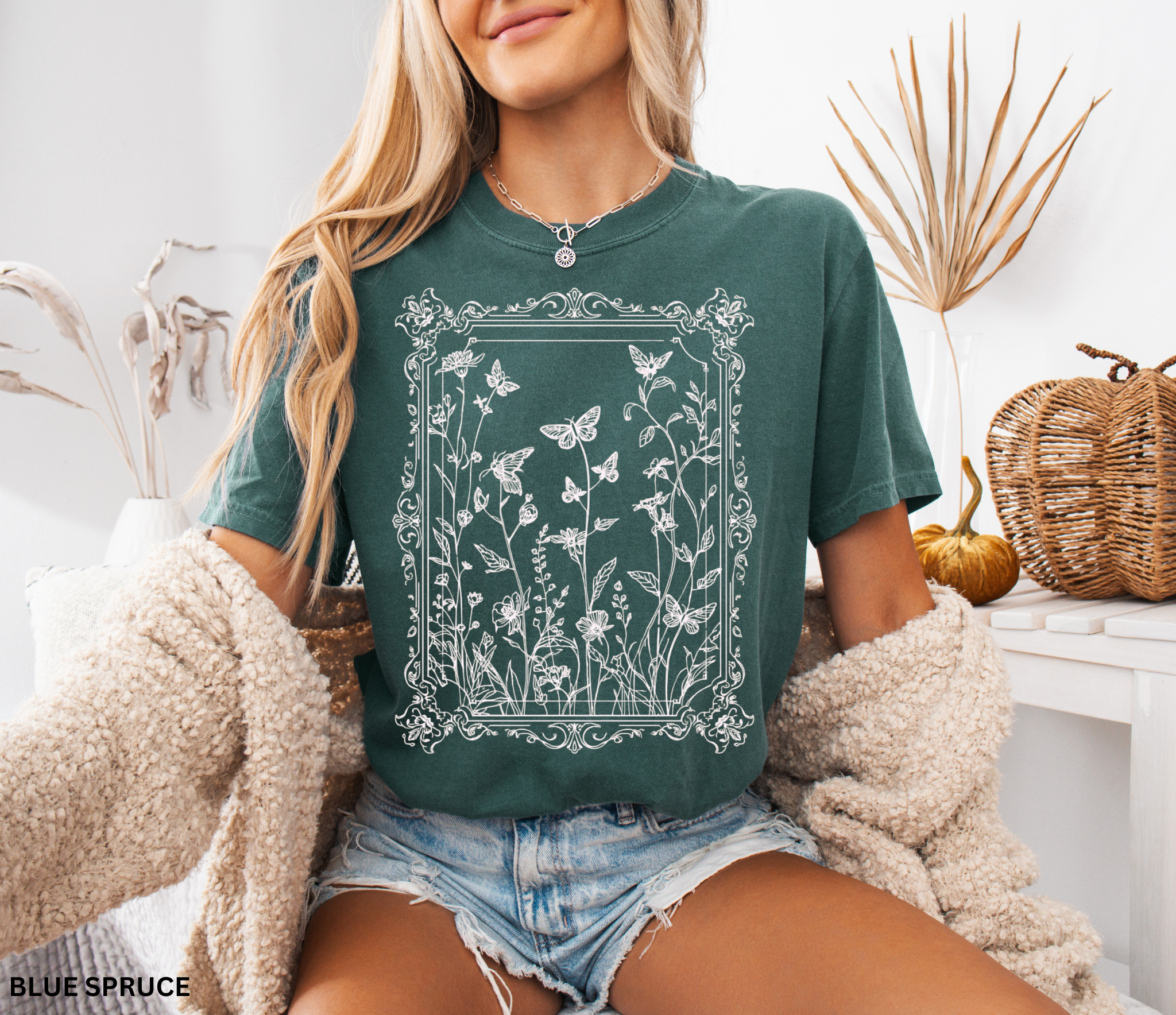 An ornate Victorian-style frame encasing hand-drawn butterflies and wildflowers on a whimsigoth-inspired cottagecore shirt.