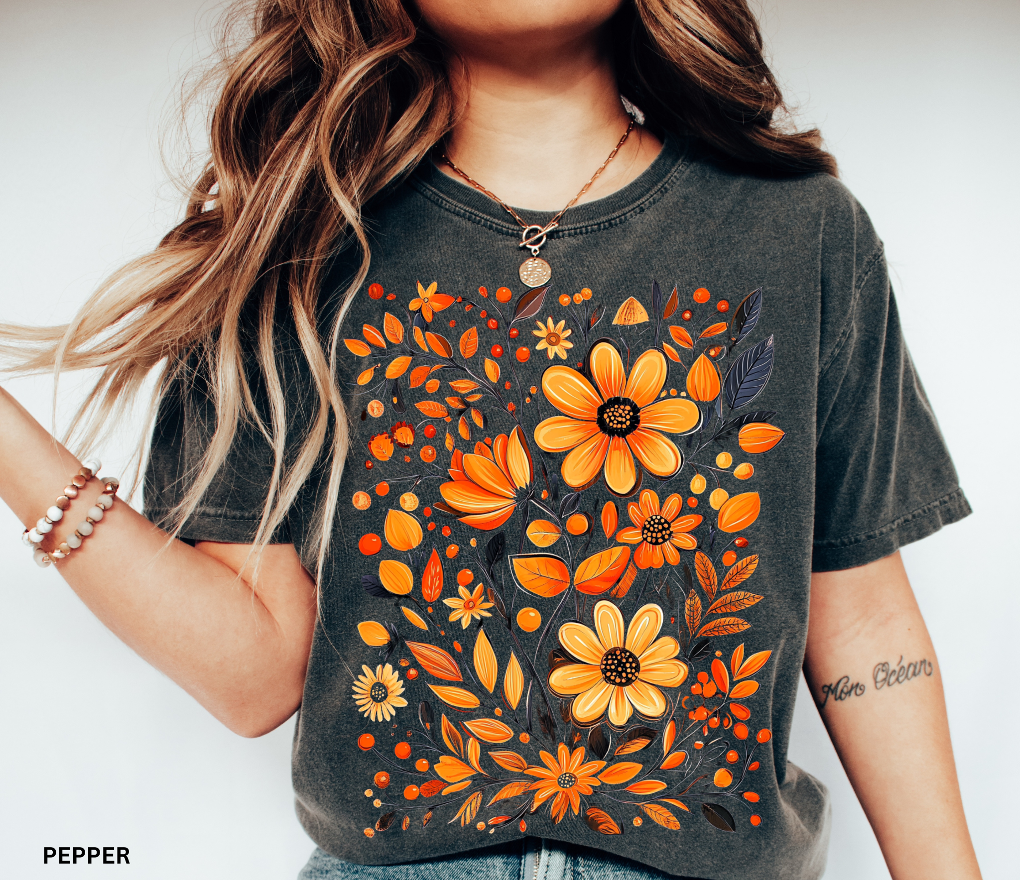 A hand-painted style floral design featuring orange and gold flowers with dark leaves, printed on a Comfort Colors cottagecore shirt.