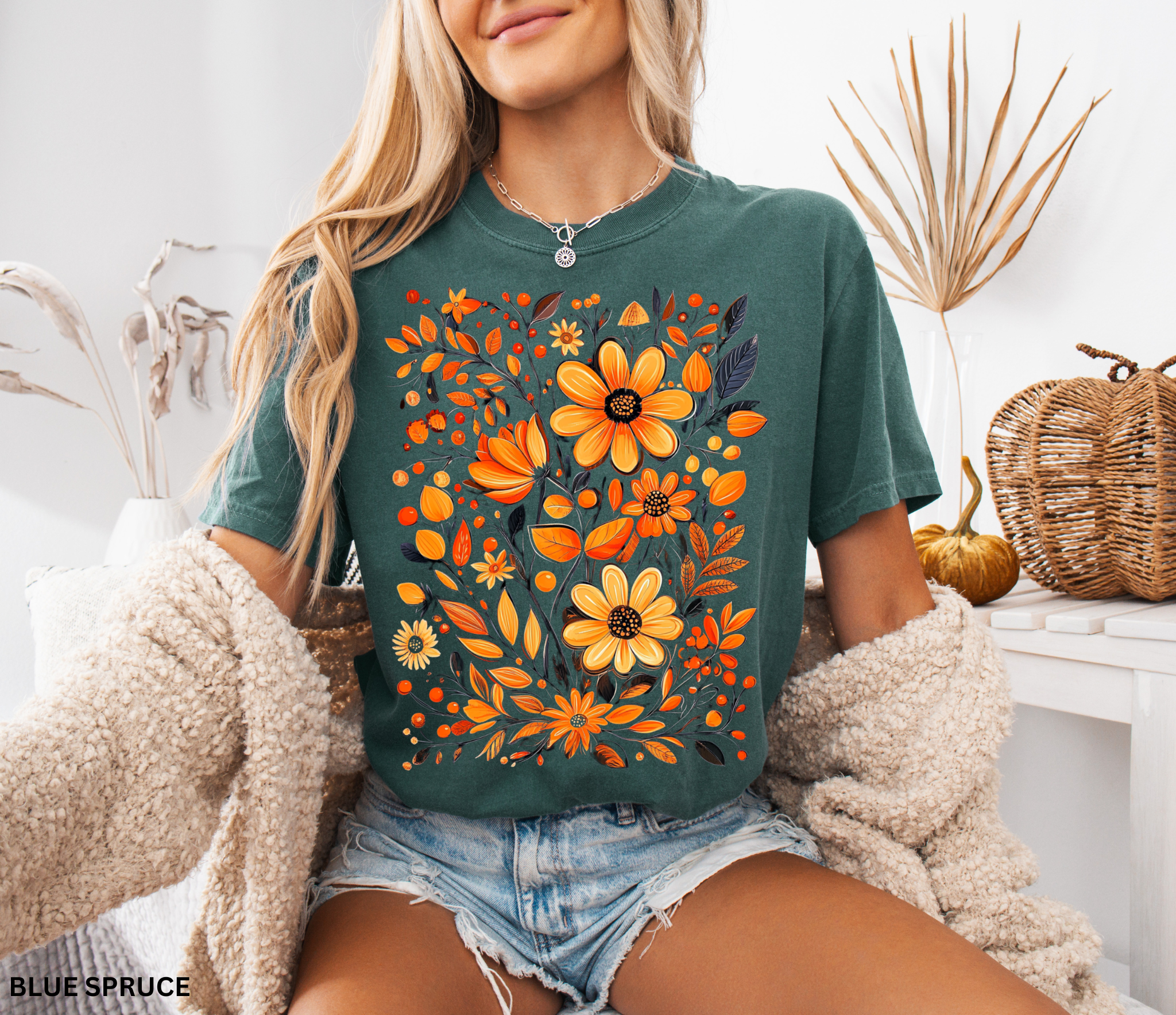 A hand-painted style floral design featuring orange and gold flowers with dark leaves, printed on a Comfort Colors cottagecore shirt.