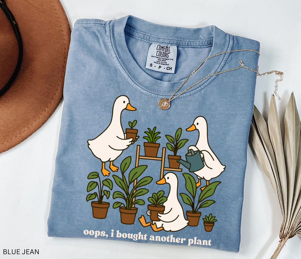 Cute shirt design featuring three geese with potted plants and the quote “Oops, I bought another plant.” Perfect for plant lovers and cottagecore style fans.
