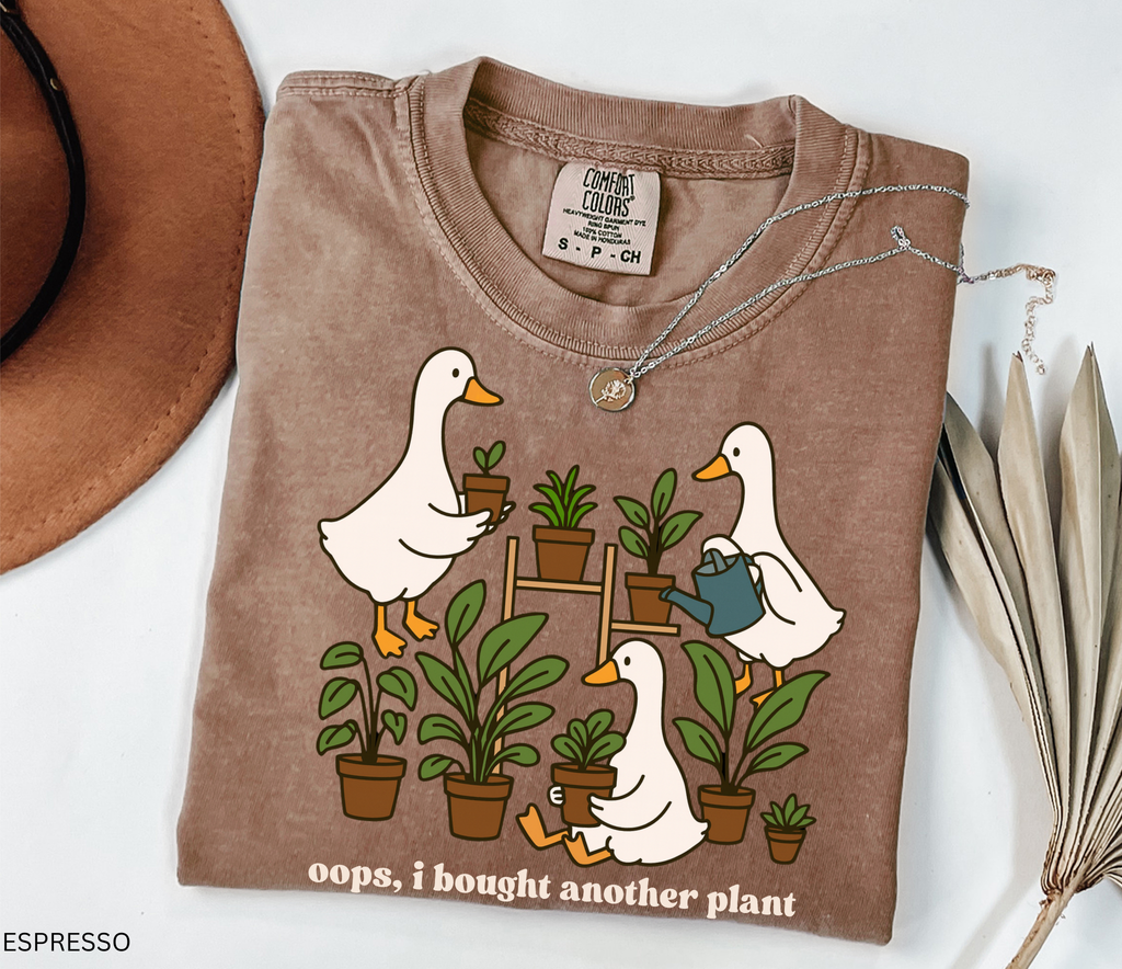 Cute shirt design featuring three geese with potted plants and the quote “Oops, I bought another plant.” Perfect for plant lovers and cottagecore style fans.