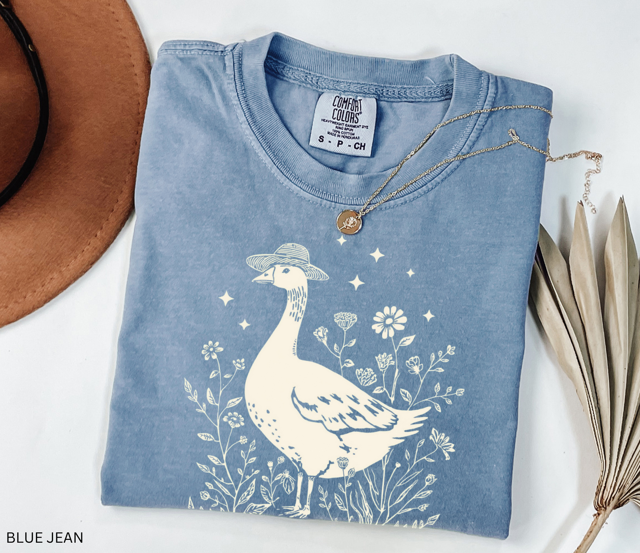 Whimsical goose wearing a straw hat surrounded by flowers and a watering can, cottagecore gardening shirt design.