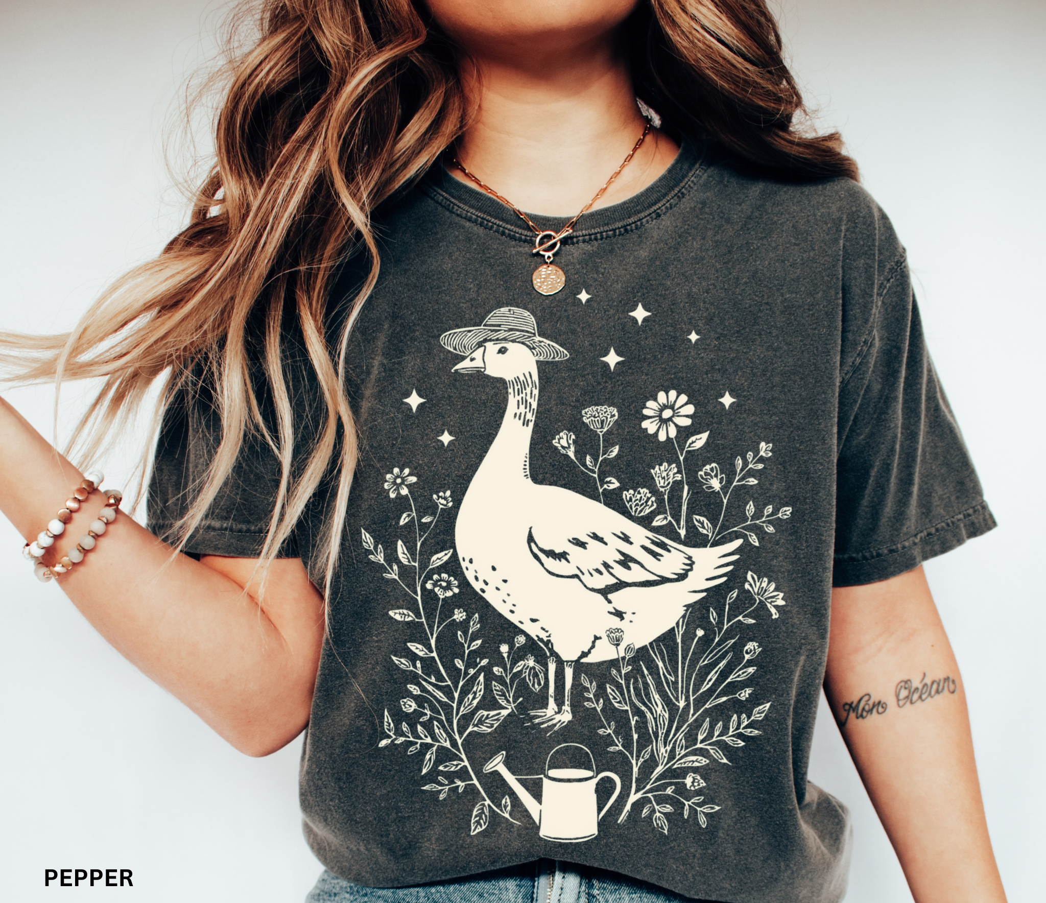 Whimsical goose wearing a straw hat surrounded by flowers and a watering can, cottagecore gardening shirt design.