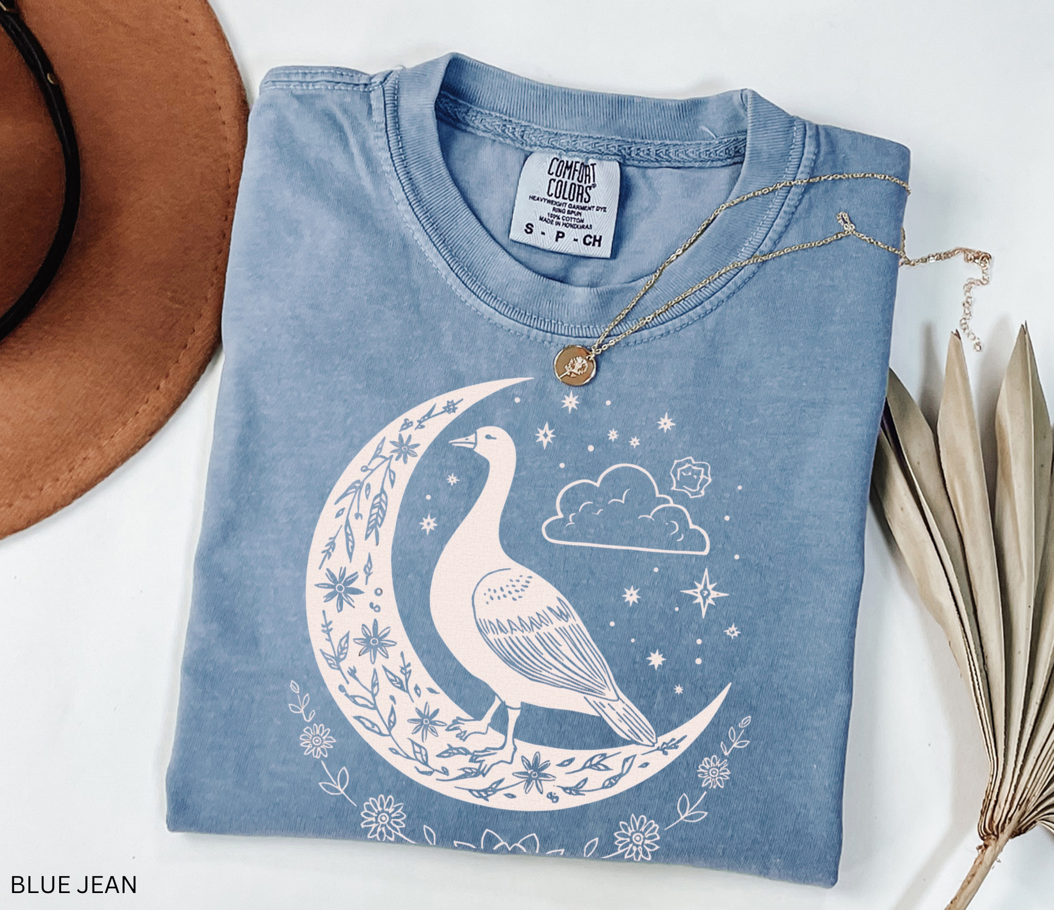 Celestial goose shirt featuring a whimsical goose on a crescent moon with stars, clouds, and floral details — witchy cottagecore design.