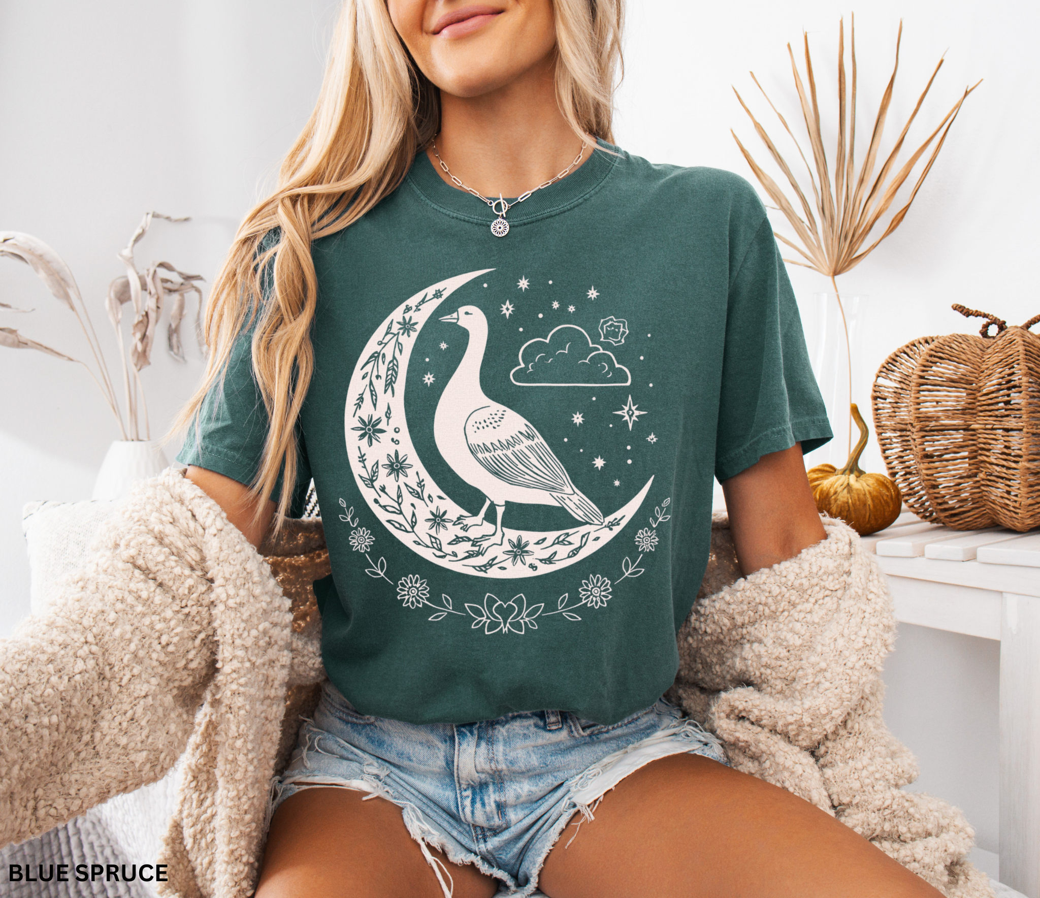 Celestial goose shirt featuring a whimsical goose on a crescent moon with stars, clouds, and floral details — witchy cottagecore design.