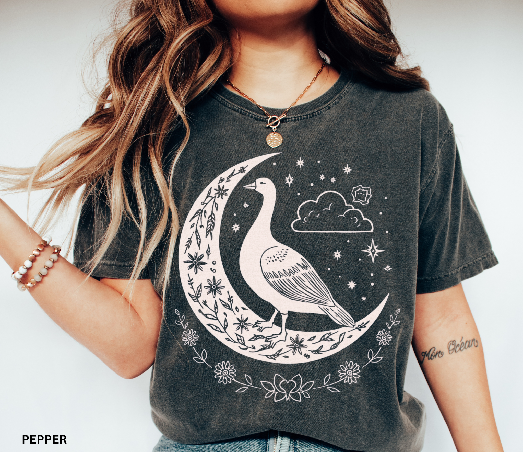 Celestial goose shirt featuring a whimsical goose on a crescent moon with stars, clouds, and floral details — witchy cottagecore design.