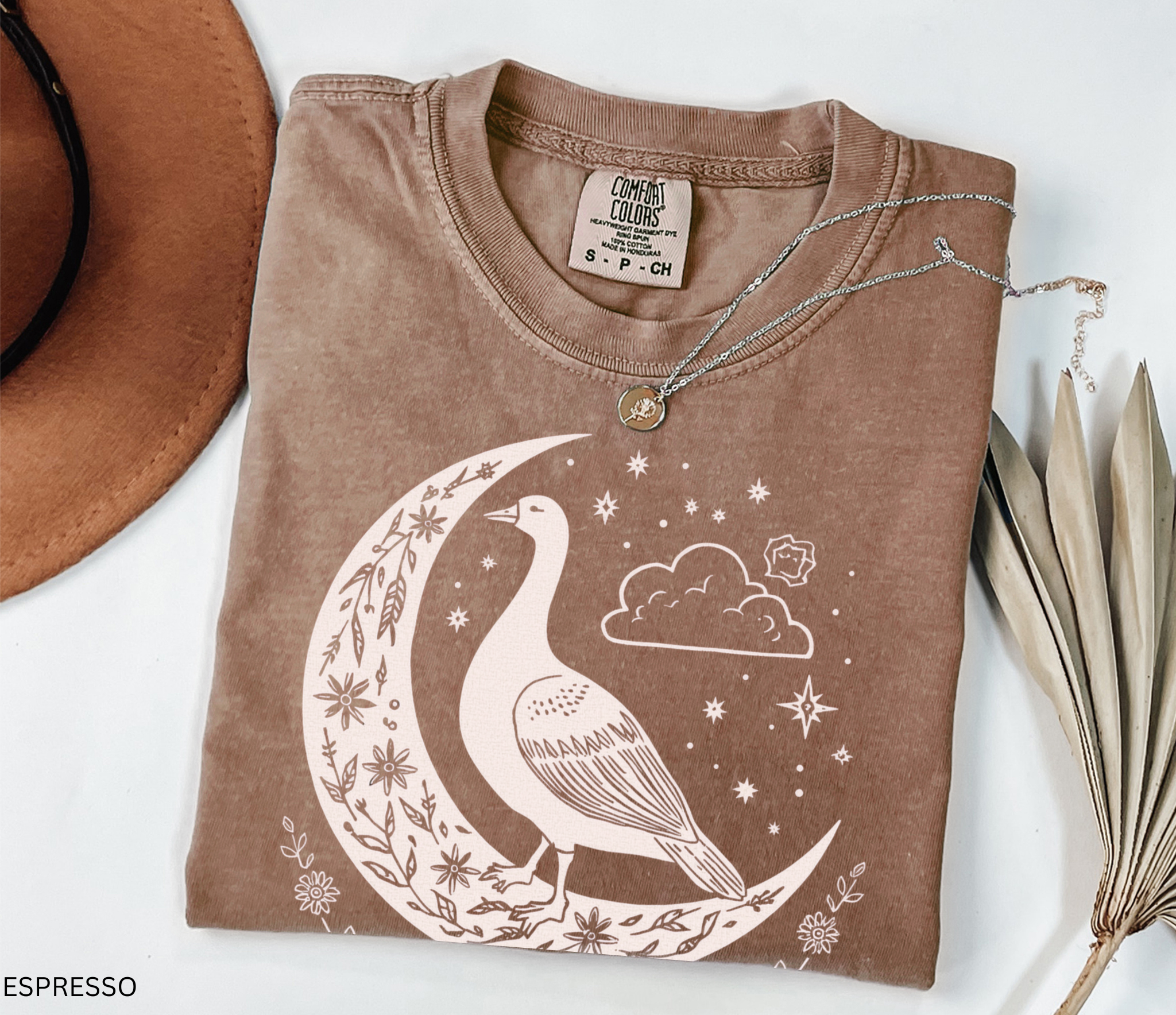 Celestial goose shirt featuring a whimsical goose on a crescent moon with stars, clouds, and floral details — witchy cottagecore design.