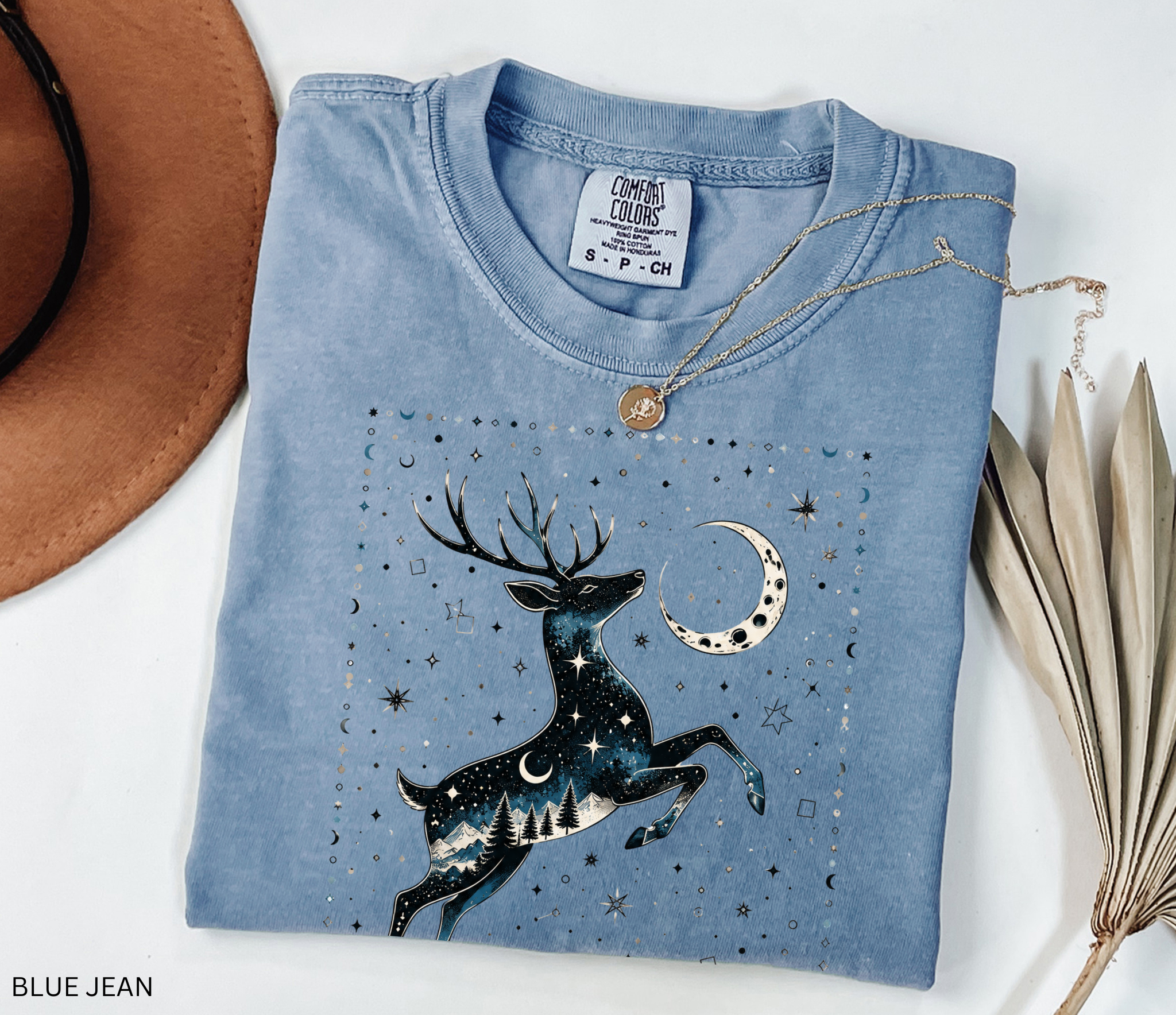 Celestial stag illustration filled with stars, moon phases, pine trees, and mountain scenery beneath a crescent moon in a mystical night-sky design.