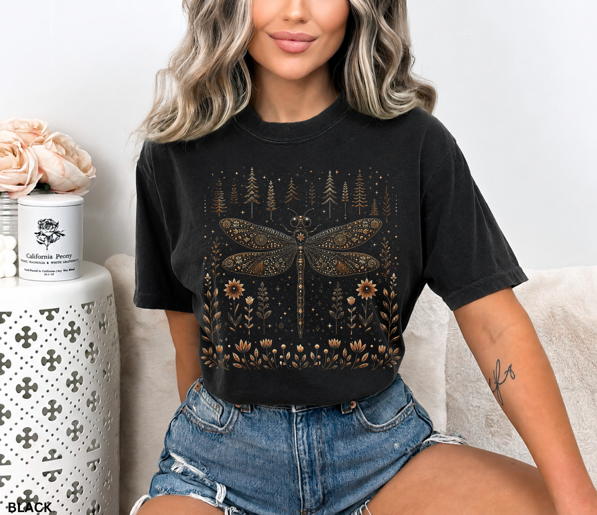 Whimsical vintage-style dragonfly illustration with intricate floral patterns on its wings, surrounded by wildflowers, pine trees, stars, and celestial details in warm bronze and cream tones against a black background.