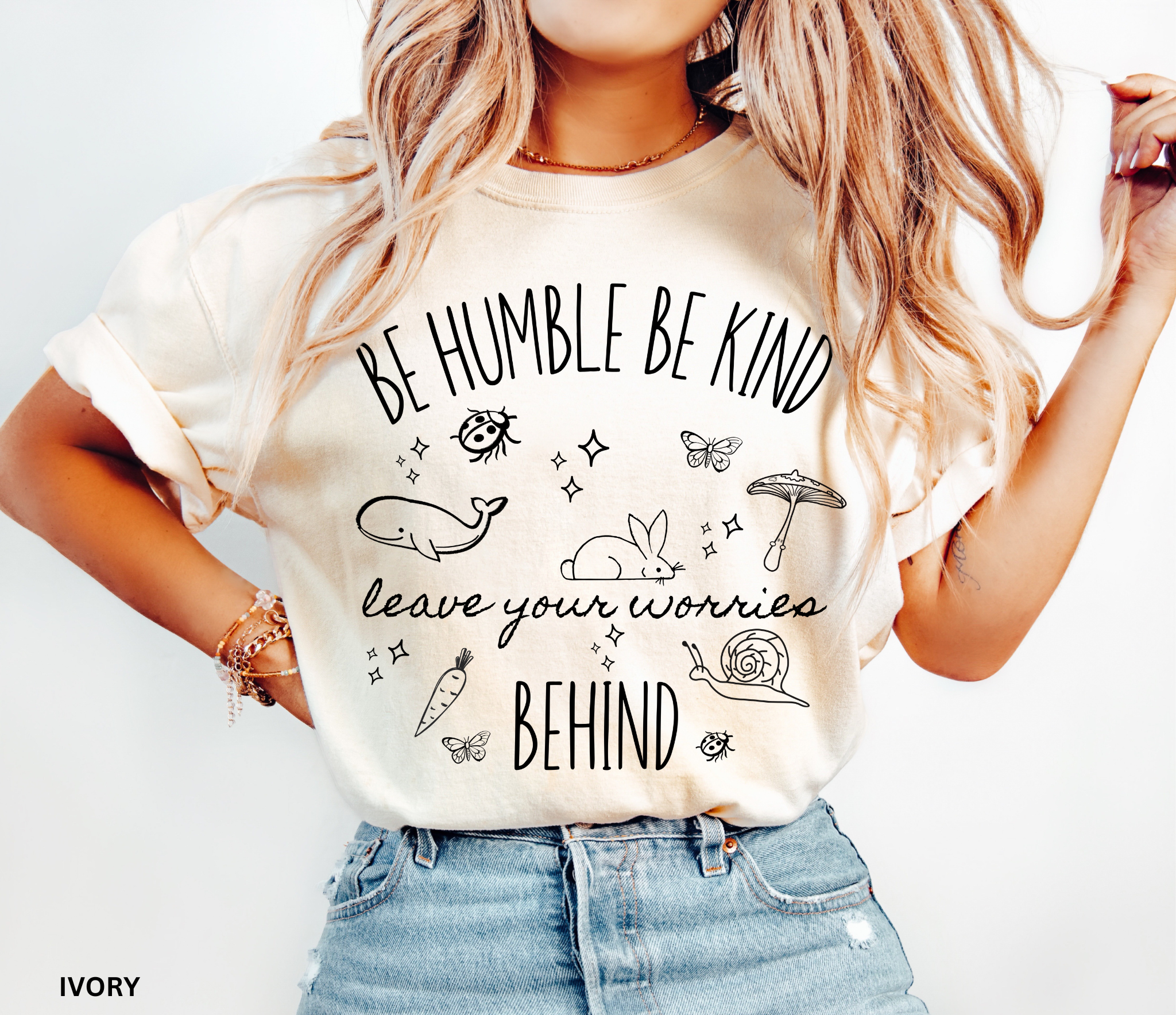 Ivory Comfort Colors shirt featuring the quote "Be Humble Be Kind Leave Your Worries Behind" surrounded by whimsical illustrations including a rabbit, whale, mushroom, snail, butterflies, and ladybugs in a cottagecore style.
