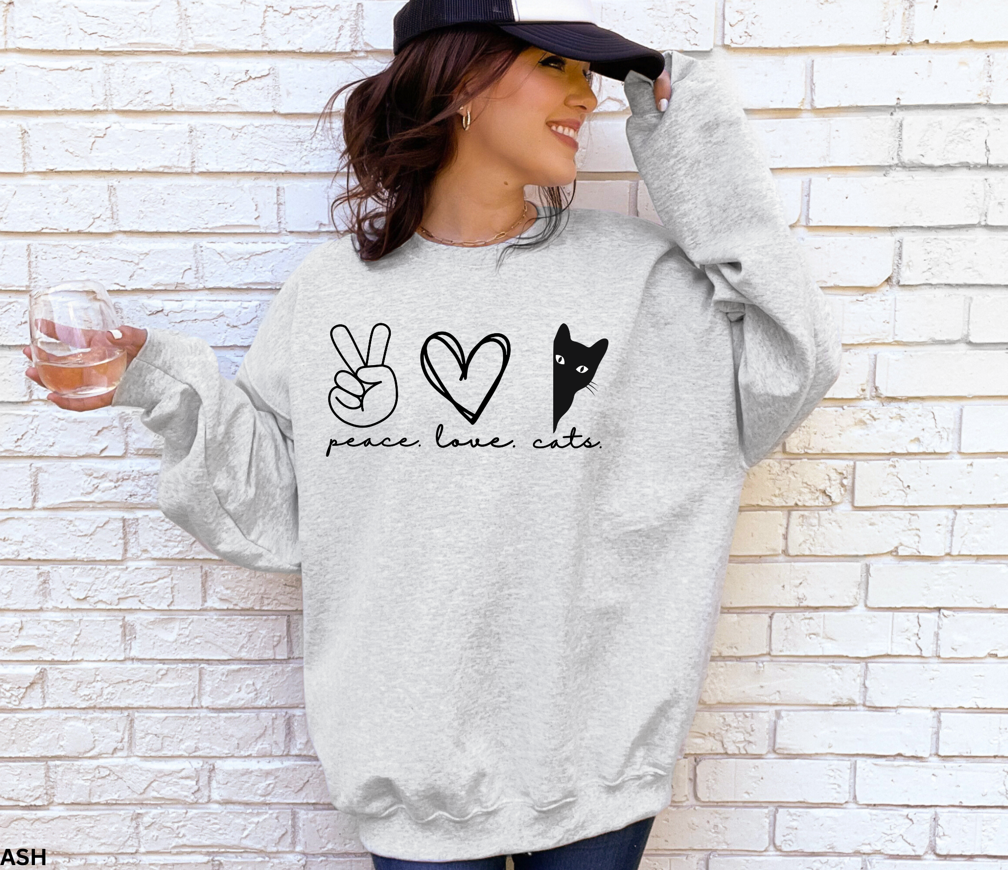 Peace Love Cats Gildan 18000 sweatshirt in sand featuring a peace sign, heart, and peeking black cat graphic, folded flat on a wood background.
