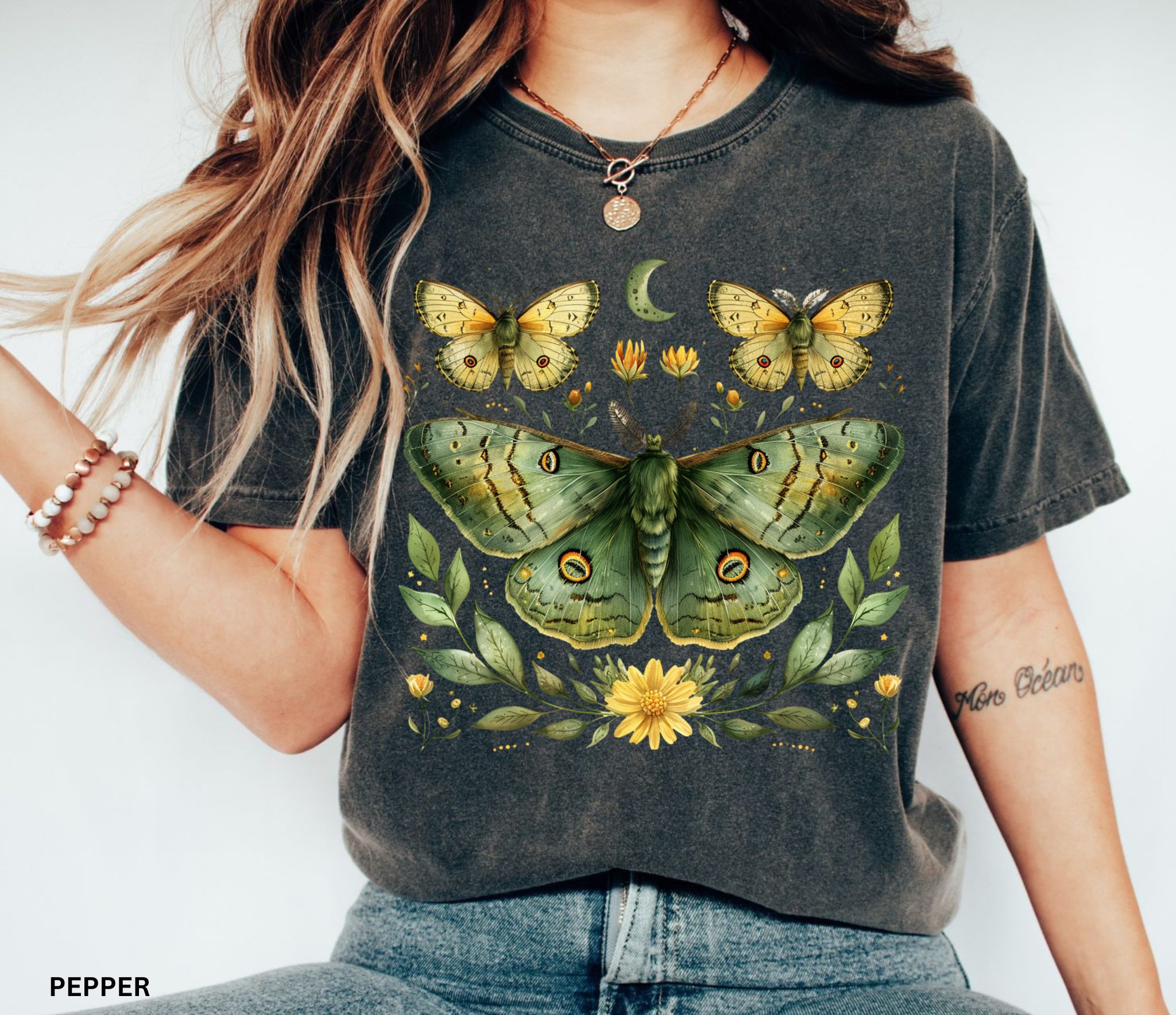 Comfort Colors graphic t-shirt featuring a detailed green luna moth surrounded by wildflowers, leaves, smaller moths, and a crescent moon in a vintage botanical cottagecore illustration