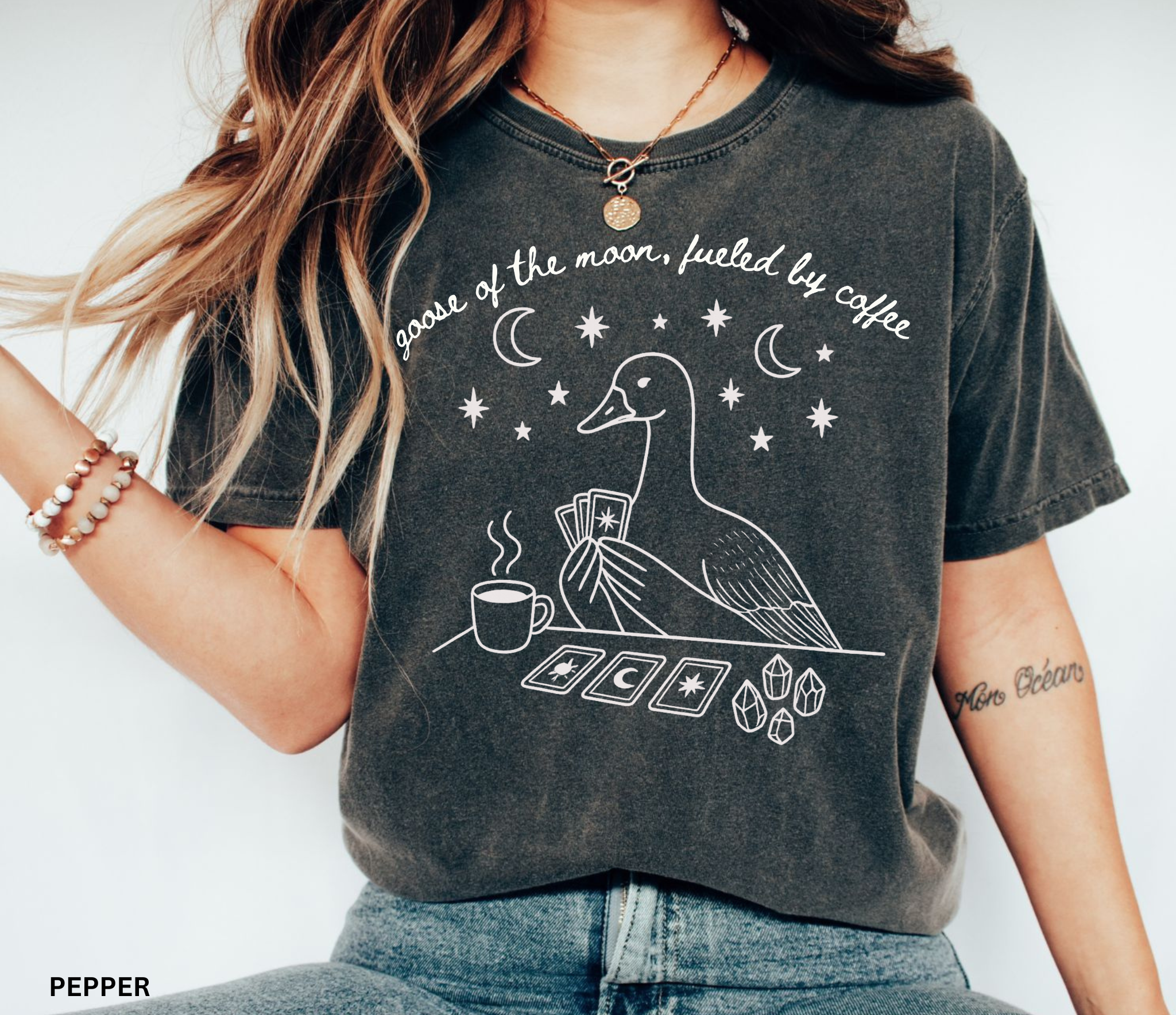Comfort Colors t-shirt featuring a celestial goose with tarot cards, coffee cup, crystals, moons and stars and the phrase "Goose of the Moon, Fueled by Coffee."
