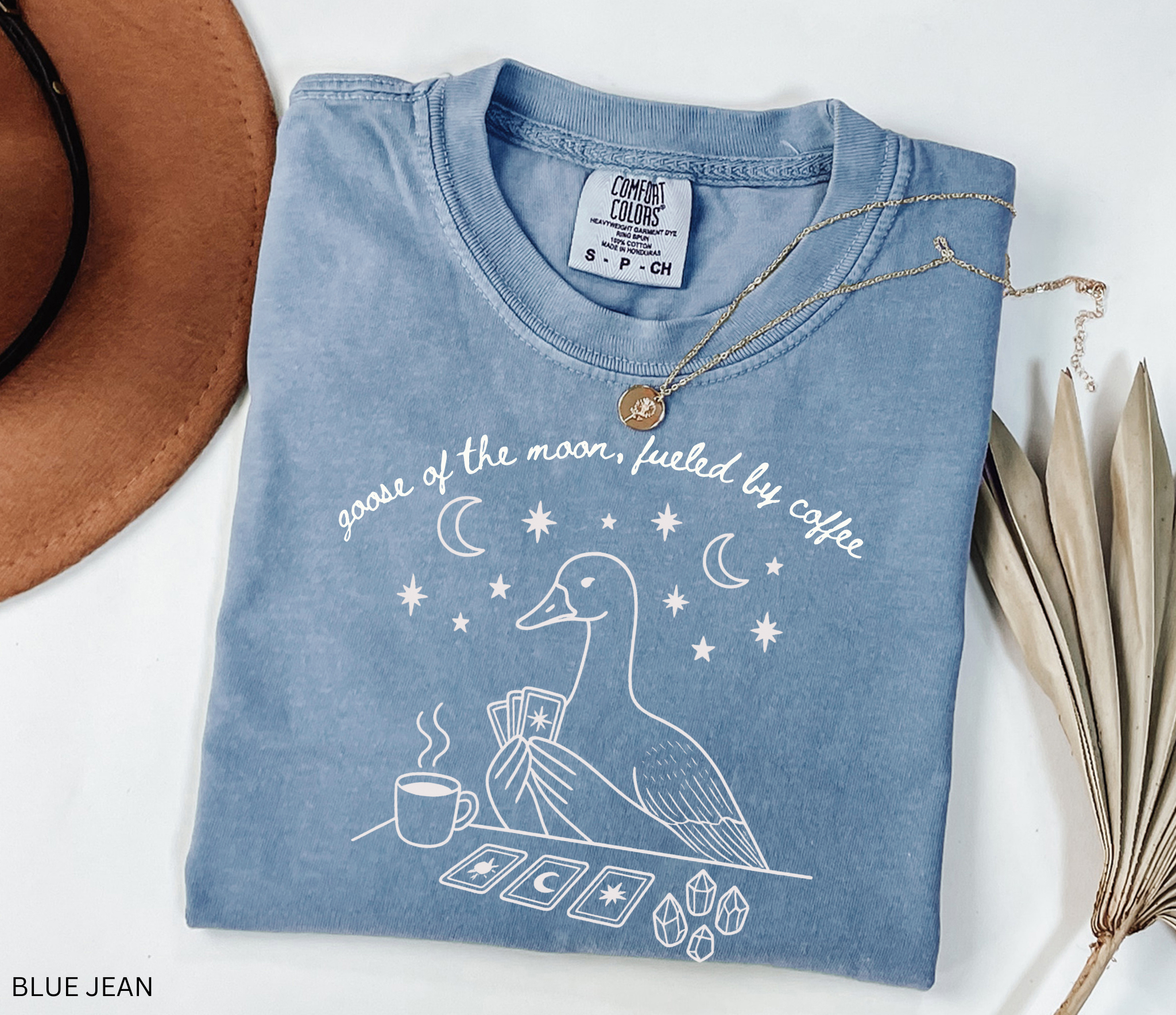 Comfort Colors t-shirt featuring a celestial goose with tarot cards, coffee cup, crystals, moons and stars and the phrase "Goose of the Moon, Fueled by Coffee."