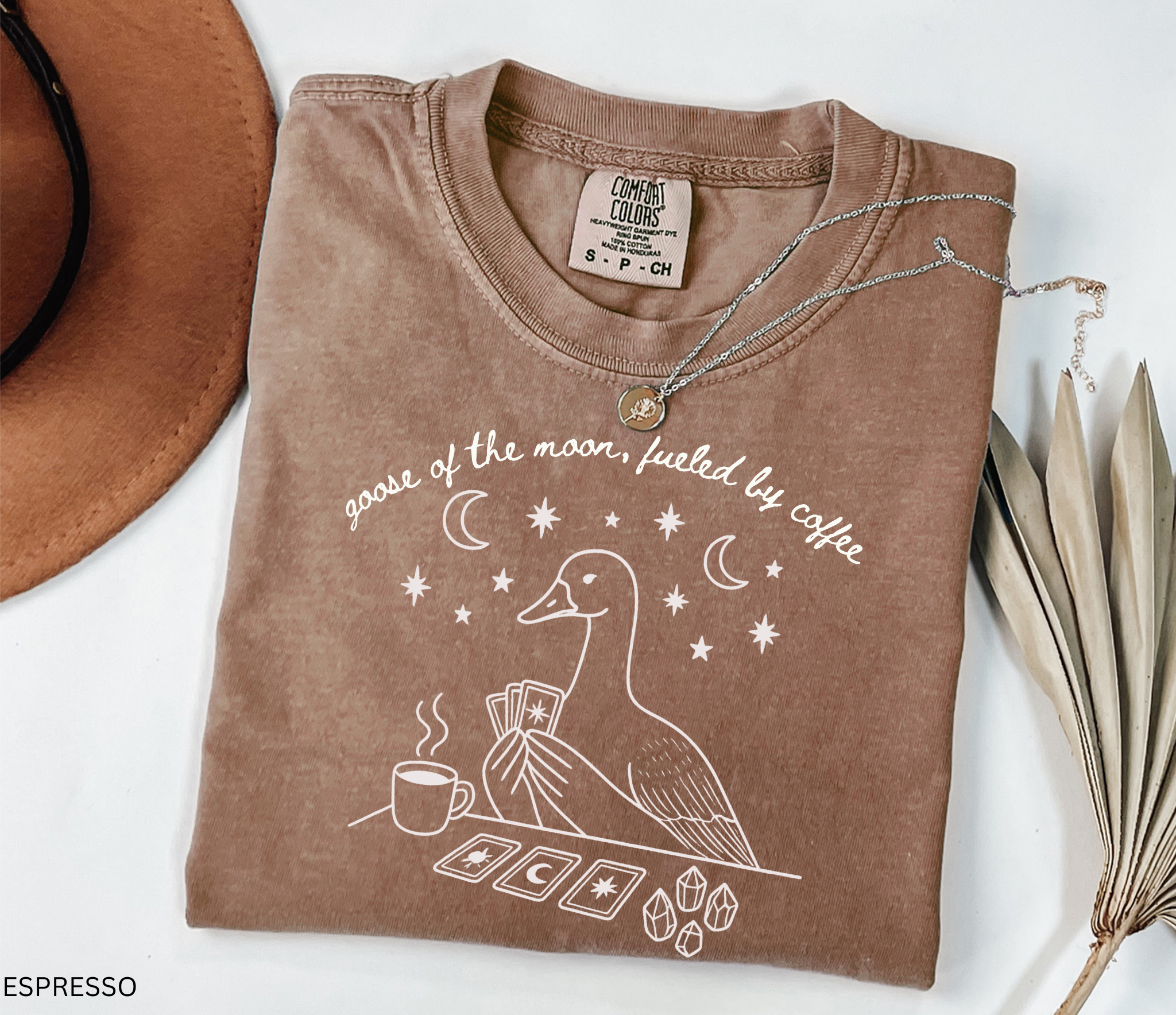 Comfort Colors t-shirt featuring a celestial goose with tarot cards, coffee cup, crystals, moons and stars and the phrase "Goose of the Moon, Fueled by Coffee."