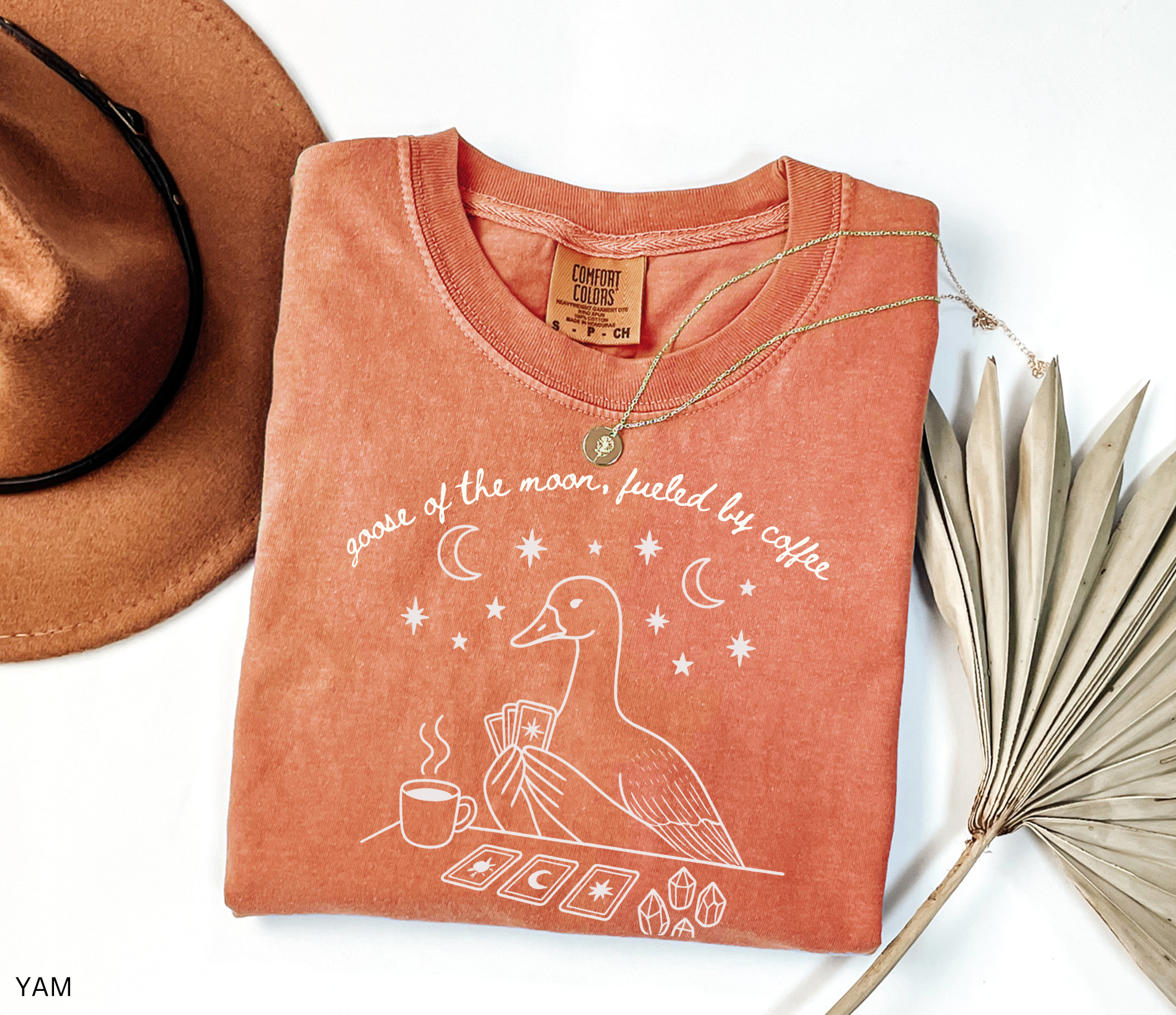 Comfort Colors t-shirt featuring a celestial goose with tarot cards, coffee cup, crystals, moons and stars and the phrase "Goose of the Moon, Fueled by Coffee."