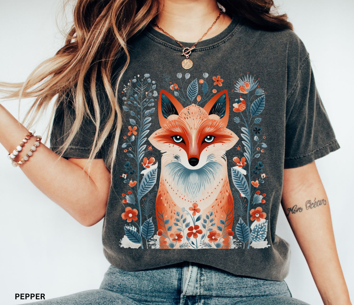 A woman wearing a dark charcoal gray graphic t-shirt with a colorful fox design, paired with blue jeans. The t-shirt has a washed, vintage texture and features a detailed illustration of a fox surrounded by flowers and leaves.